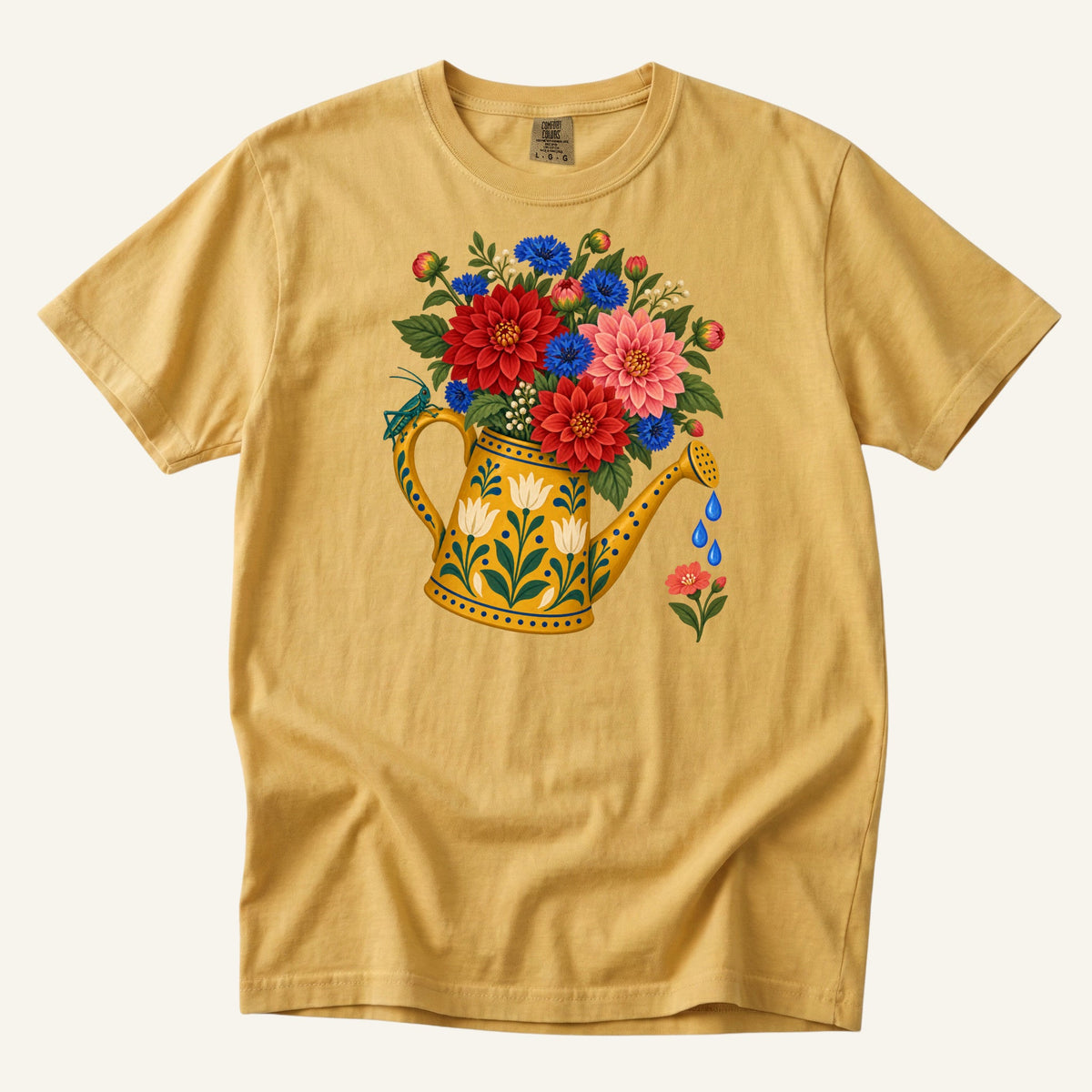 Folk Art collection — a golden watering can holding red, pink and blue blooms on a mustard garment-dyed tee