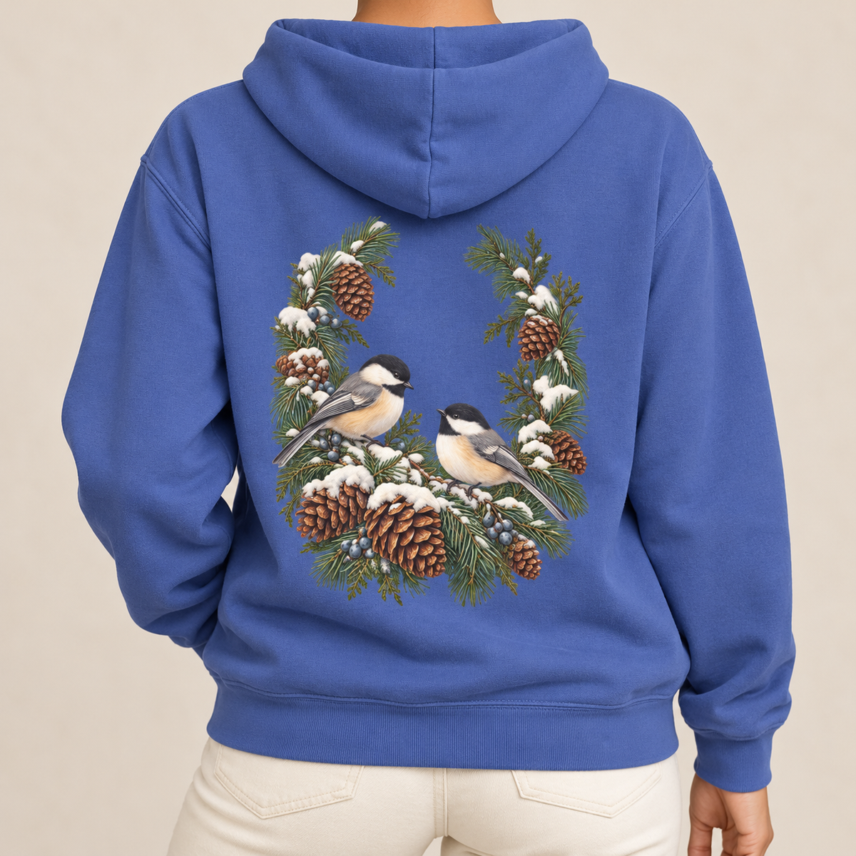 Winter Chickadee hoodie in Flo Blue worn, close view of the back print with two chickadees inside a snowy pine and pinecone wreath