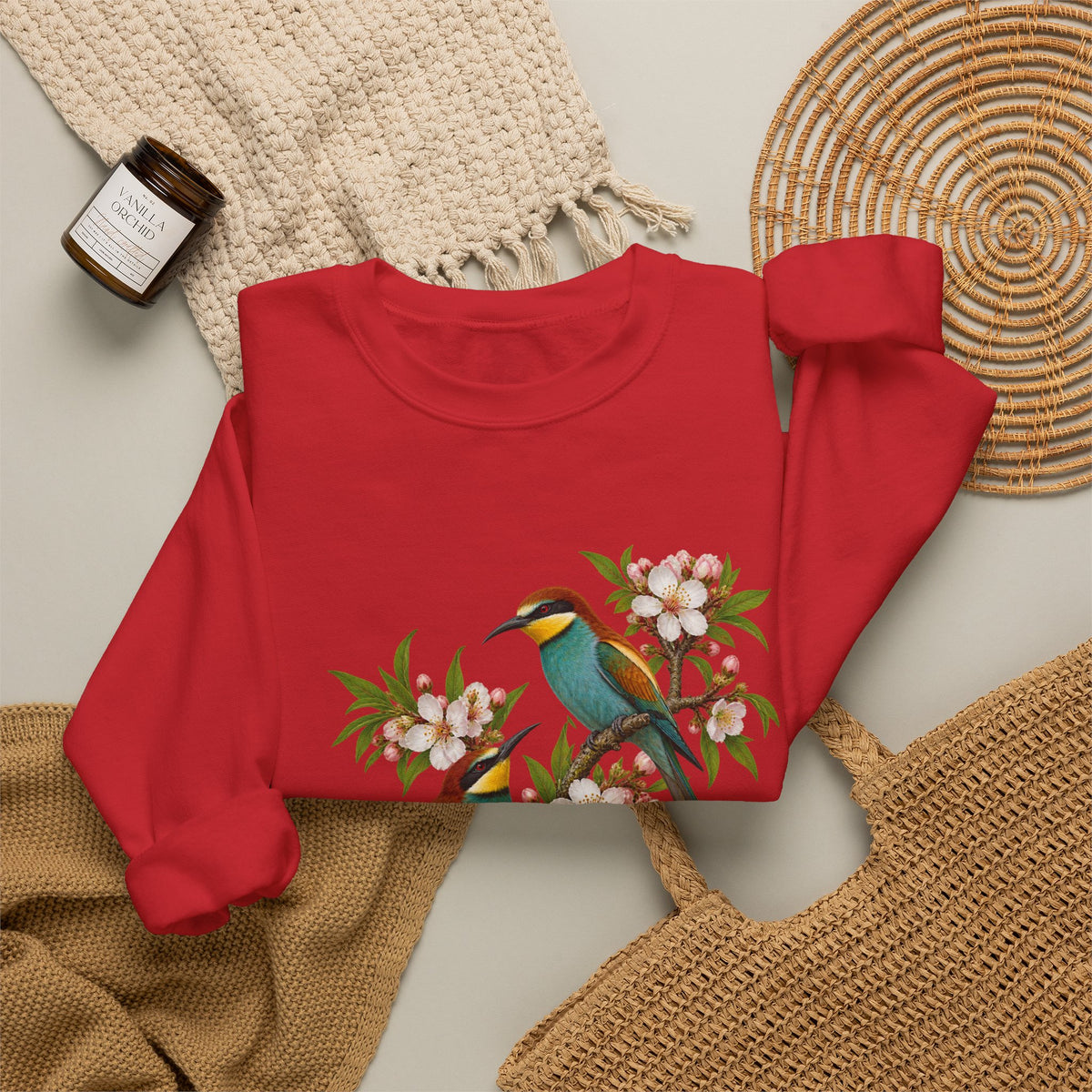 The Scenic Way Home sweatshirt — two birds with teal, golden-yellow and rust plumage perched among cream and blush blossoms, on a unisex crewneck
