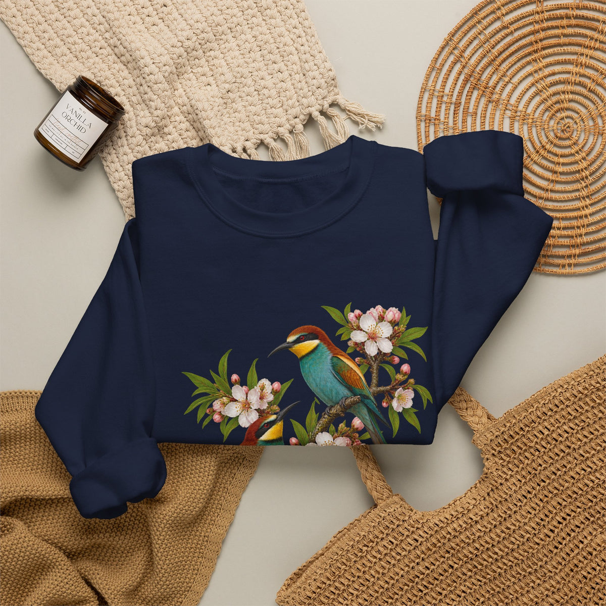 The Scenic Way Home sweatshirt — two birds with teal, golden-yellow and rust plumage perched among cream and blush blossoms, on a unisex crewneck