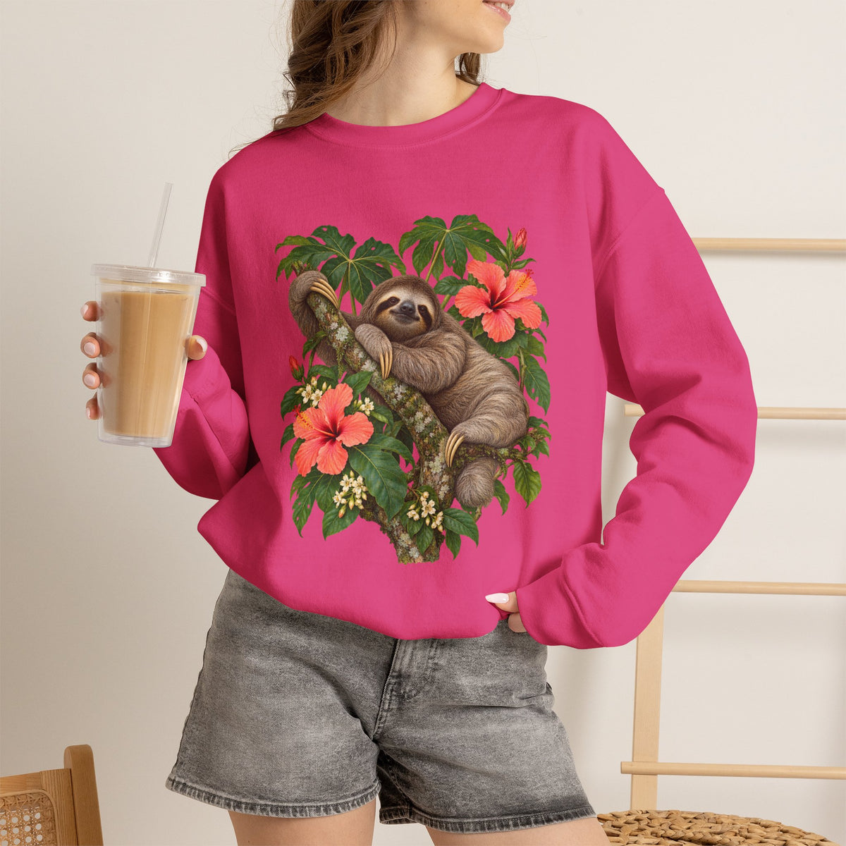 Taking My Sweet Time sweatshirt — a sloth resting on a mossy branch among coral hibiscus, cream blossoms and tropical leaves, on a unisex crewneck