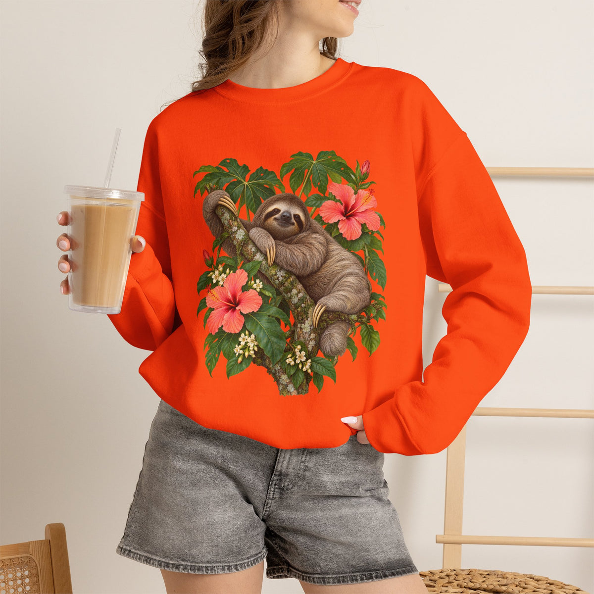 Taking My Sweet Time sweatshirt — a sloth resting on a mossy branch among coral hibiscus, cream blossoms and tropical leaves, on a unisex crewneck