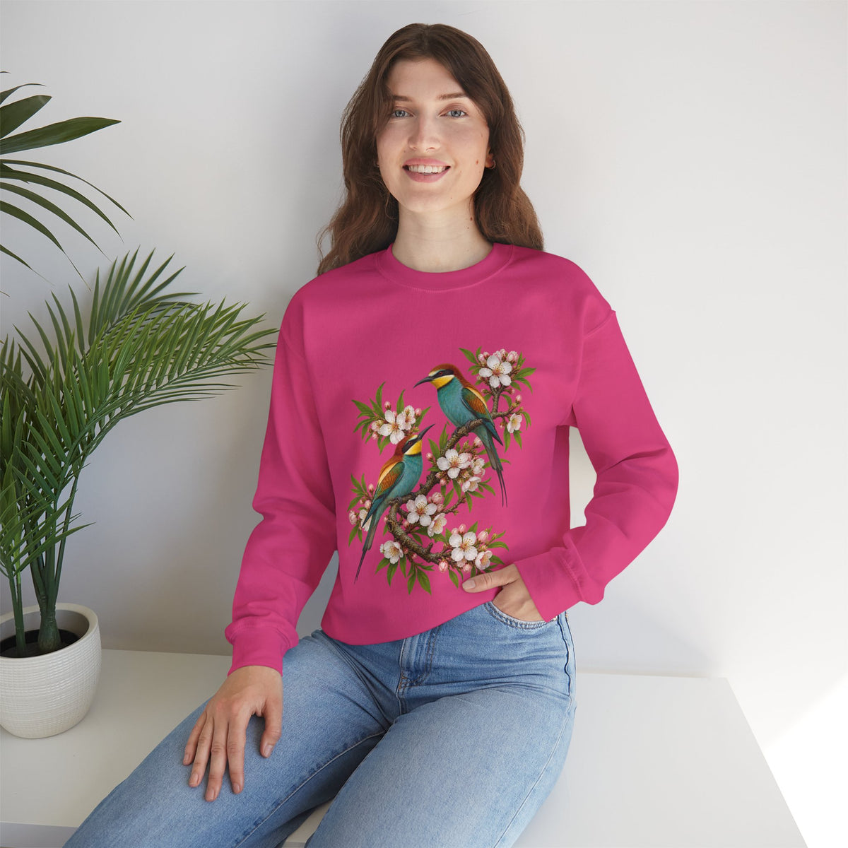 The Scenic Way Home sweatshirt — two birds with teal, golden-yellow and rust plumage perched among cream and blush blossoms, on a unisex crewneck