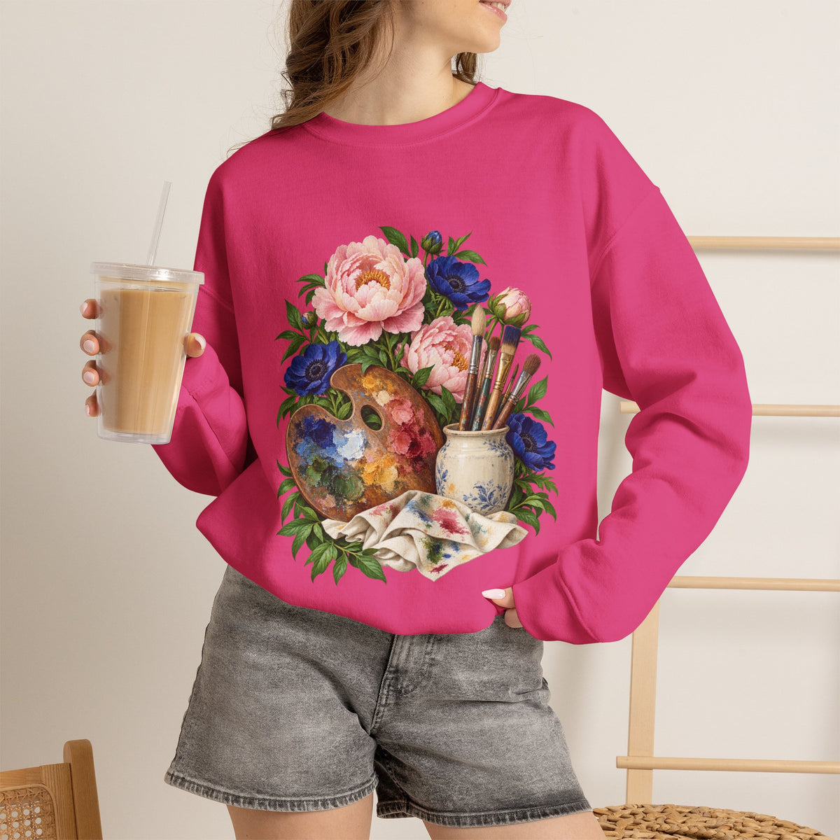 The Colors She Kept crewneck sweatshirt, a paint-covered artist palette beside a cream ceramic jar of brushes with pink peonies and deep blue flowers, image 13 of 28