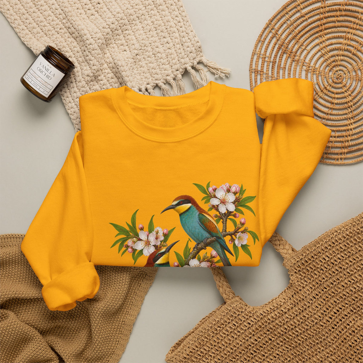 The Scenic Way Home sweatshirt — two birds with teal, golden-yellow and rust plumage perched among cream and blush blossoms, on a unisex crewneck