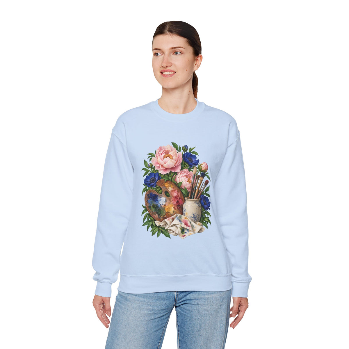 The Colors She Kept crewneck sweatshirt, a paint-covered artist palette beside a cream ceramic jar of brushes with pink peonies and deep blue flowers, image 18 of 28