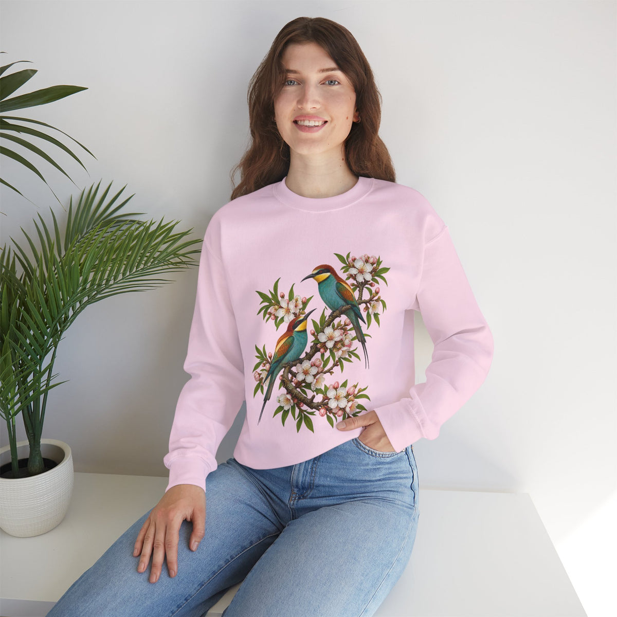 The Scenic Way Home sweatshirt — two birds with teal, golden-yellow and rust plumage perched among cream and blush blossoms, on a unisex crewneck