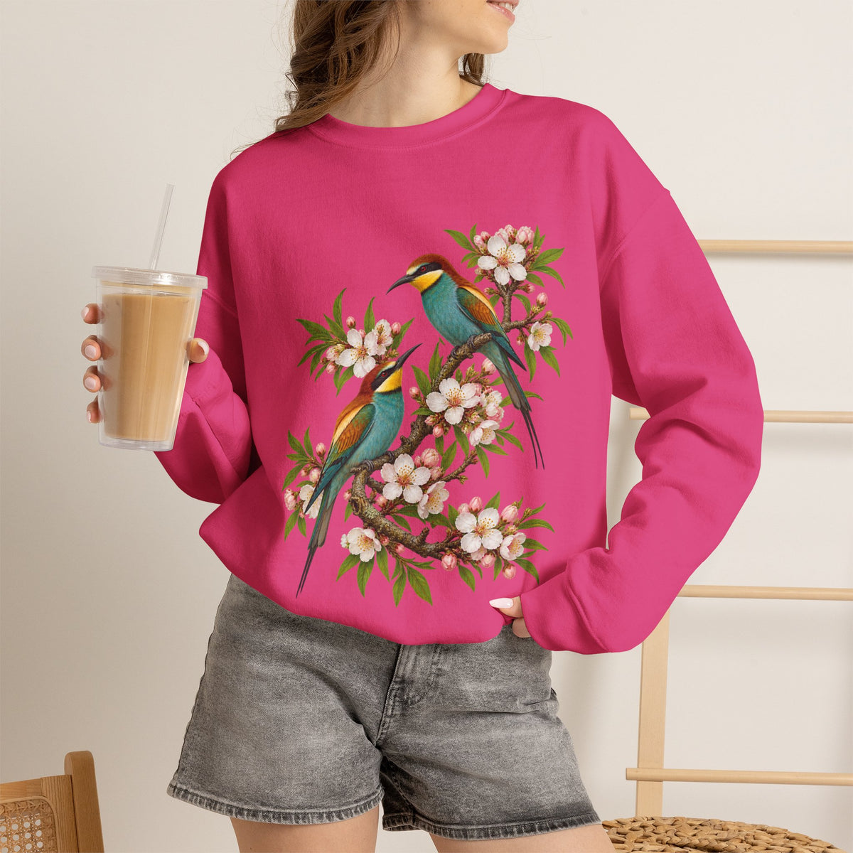 The Scenic Way Home sweatshirt — two birds with teal, golden-yellow and rust plumage perched among cream and blush blossoms, on a unisex crewneck
