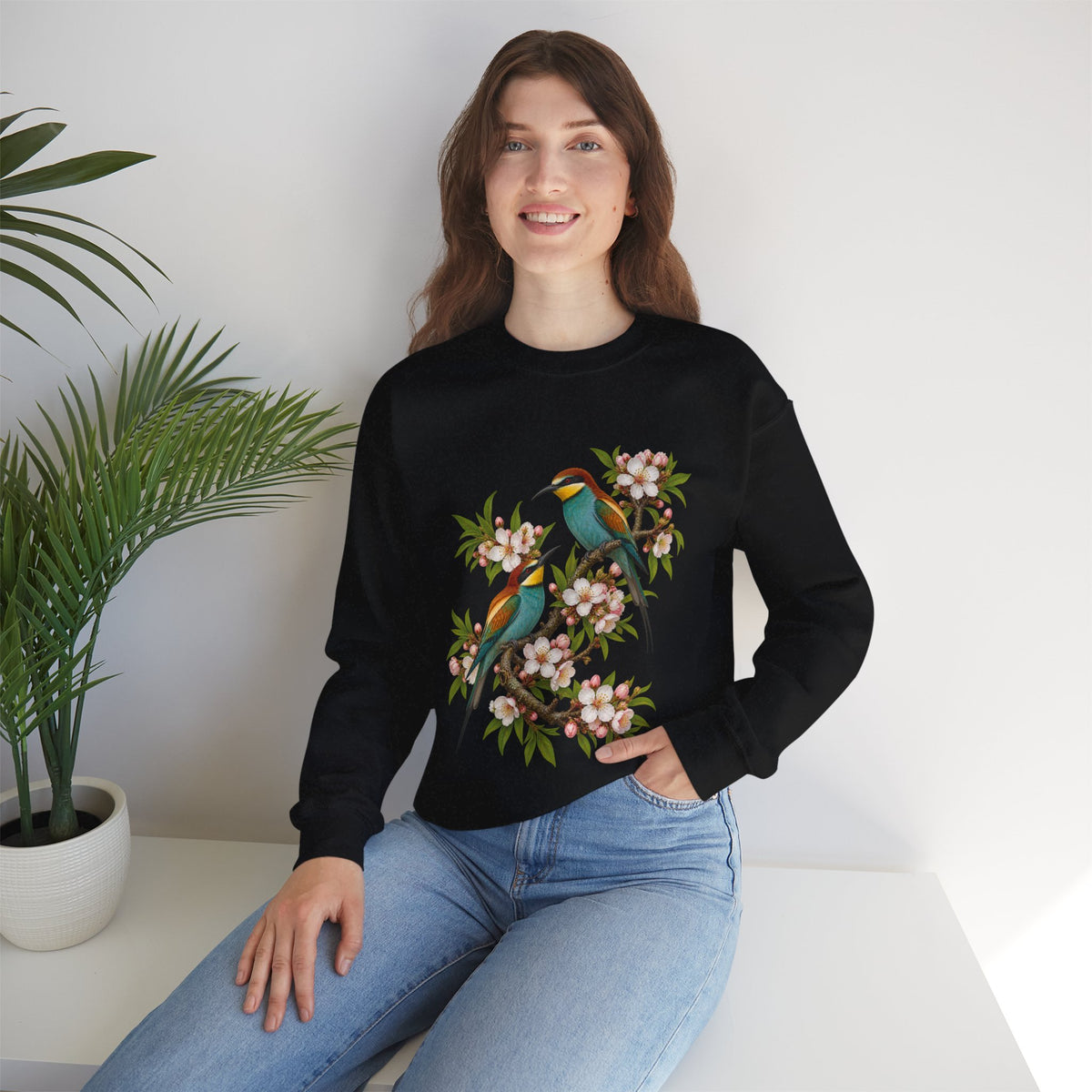 The Scenic Way Home sweatshirt — two birds with teal, golden-yellow and rust plumage perched among cream and blush blossoms, on a unisex crewneck