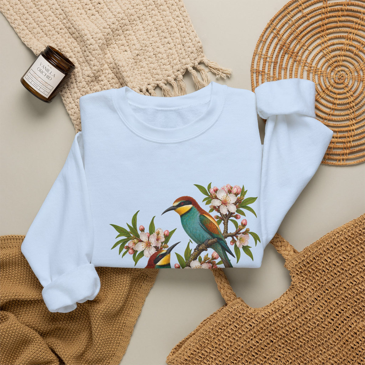 The Scenic Way Home sweatshirt — two birds with teal, golden-yellow and rust plumage perched among cream and blush blossoms, on a unisex crewneck