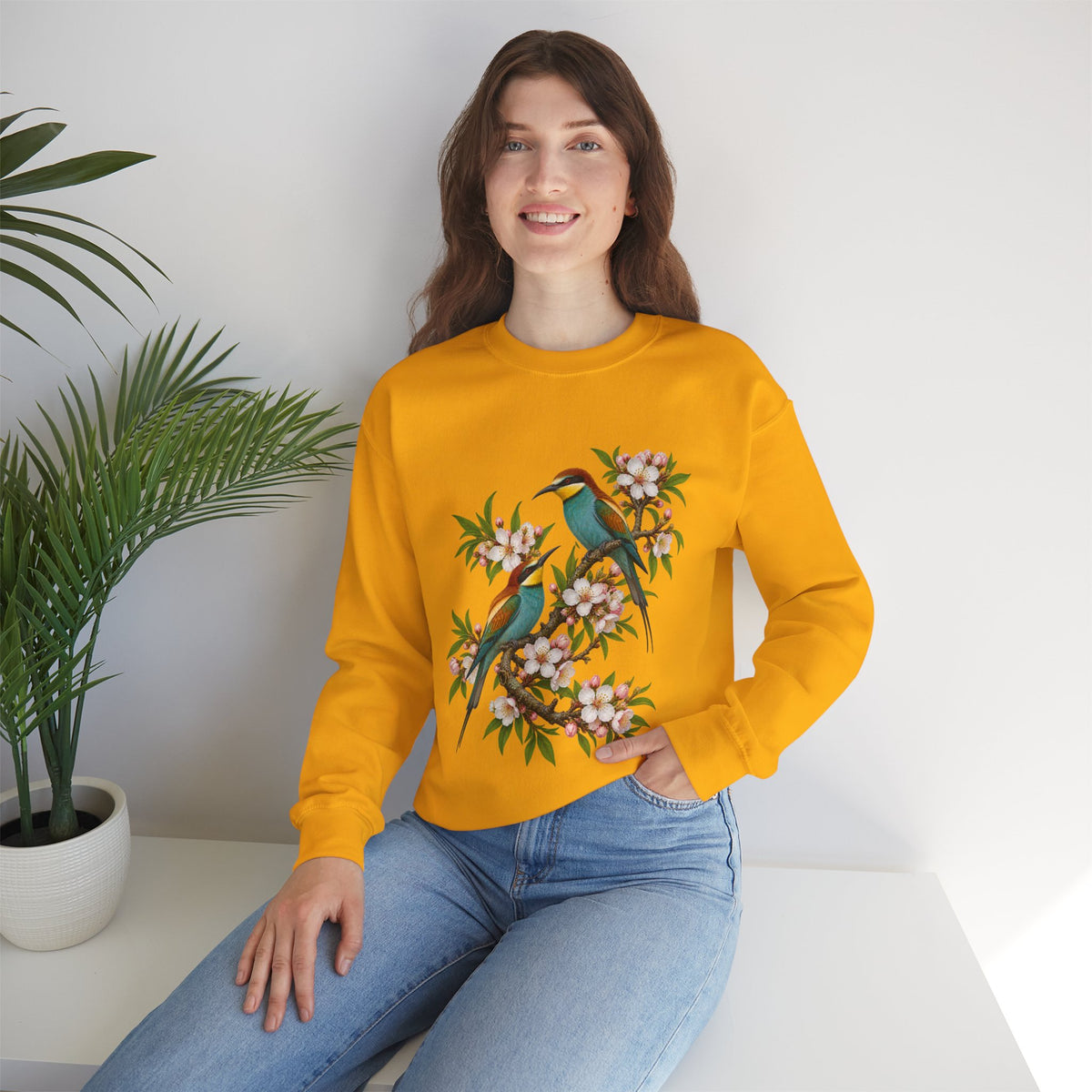 The Scenic Way Home sweatshirt — two birds with teal, golden-yellow and rust plumage perched among cream and blush blossoms, on a unisex crewneck