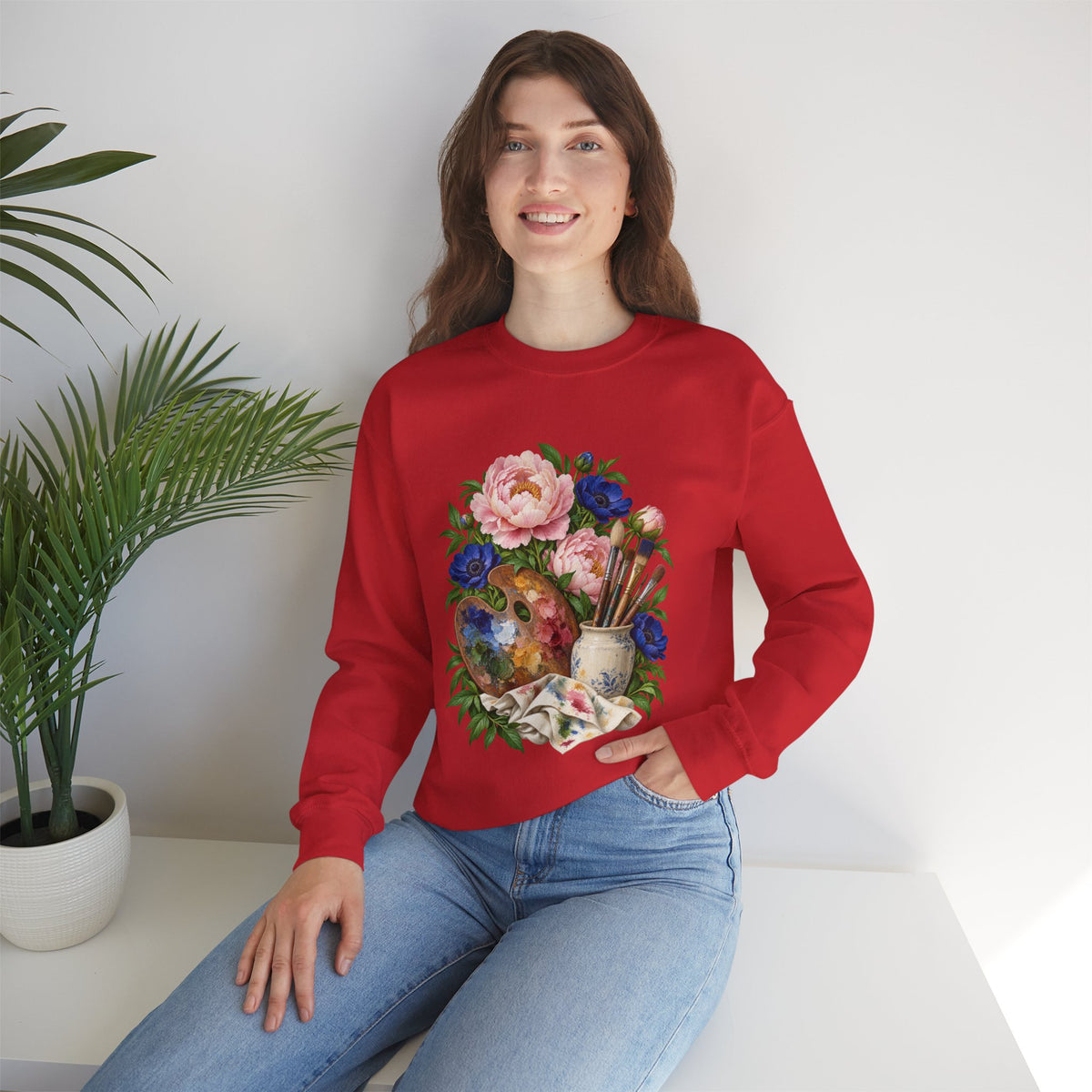 The Colors She Kept crewneck sweatshirt, a paint-covered artist palette beside a cream ceramic jar of brushes with pink peonies and deep blue flowers, image 9 of 28