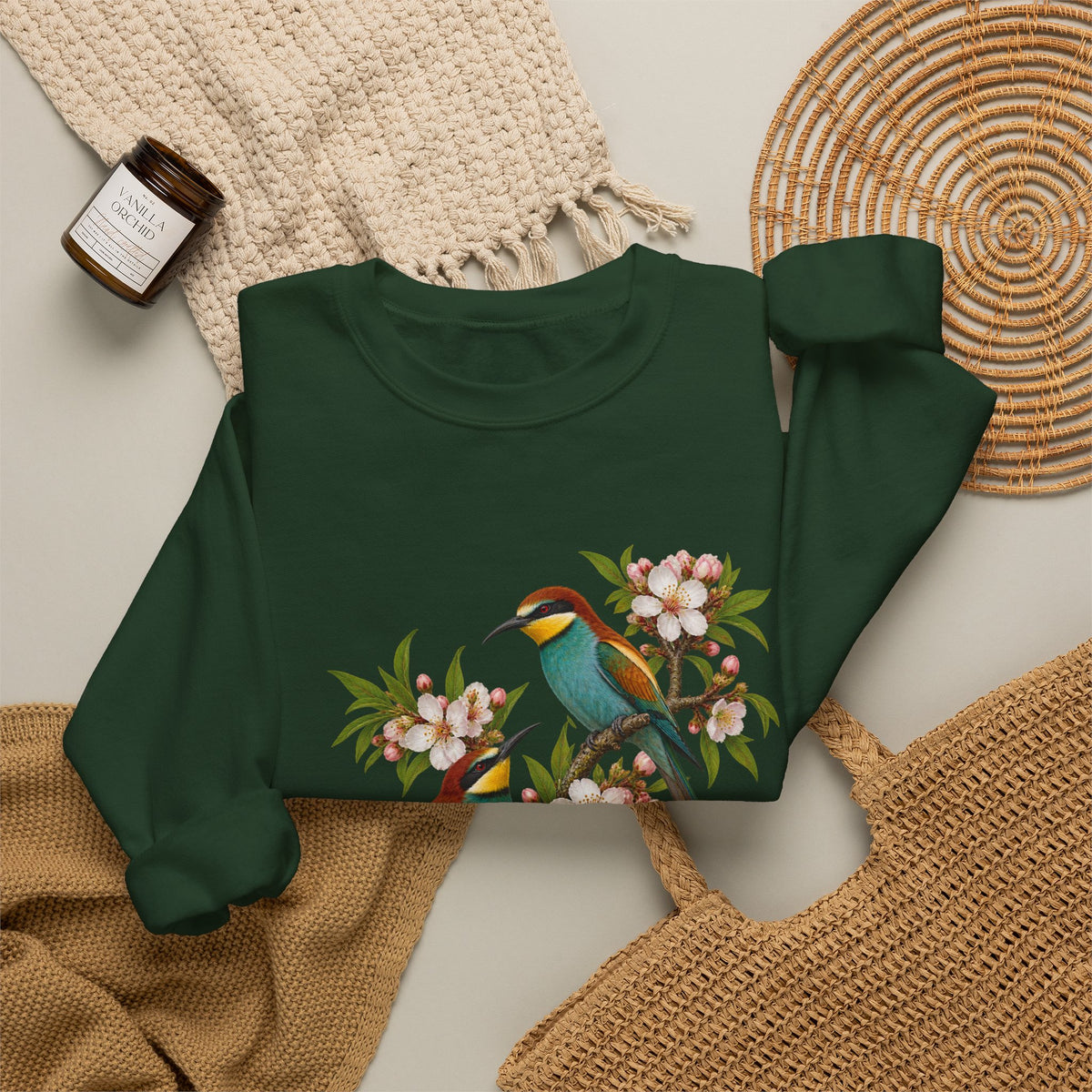 The Scenic Way Home sweatshirt — two birds with teal, golden-yellow and rust plumage perched among cream and blush blossoms, on a unisex crewneck