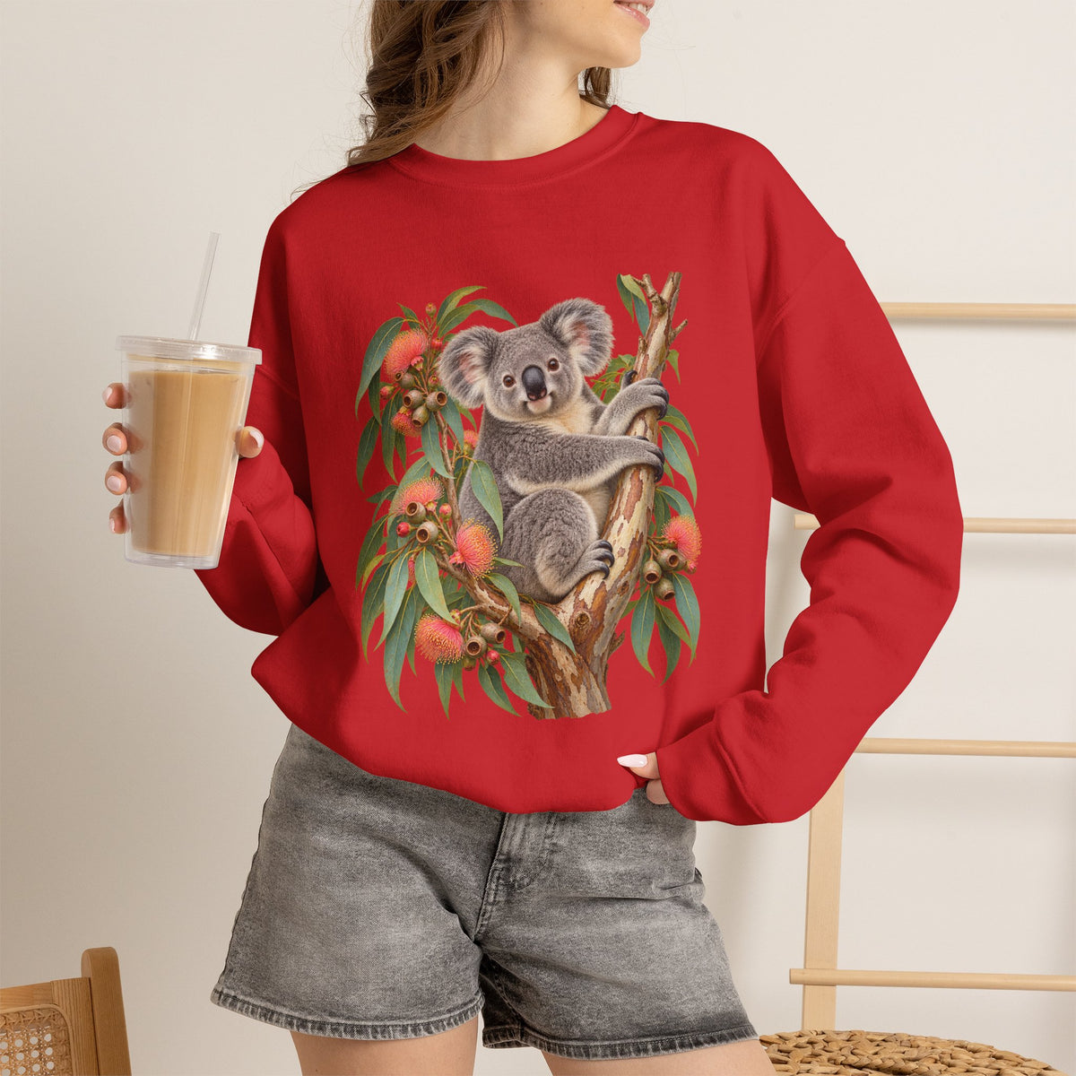Booked for the Afternoon sweatshirt — a grey koala resting among eucalyptus leaves and coral-pink blossoms, on a unisex crewneck