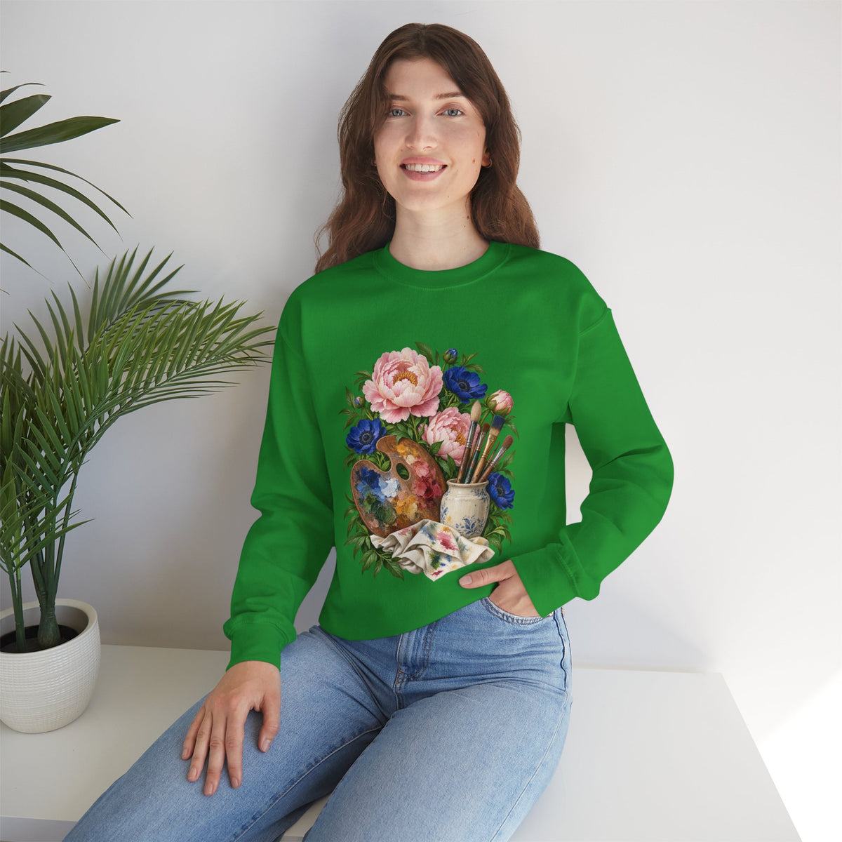 The Colors She Kept crewneck sweatshirt, a paint-covered artist palette beside a cream ceramic jar of brushes with pink peonies and deep blue flowers, image 15 of 28