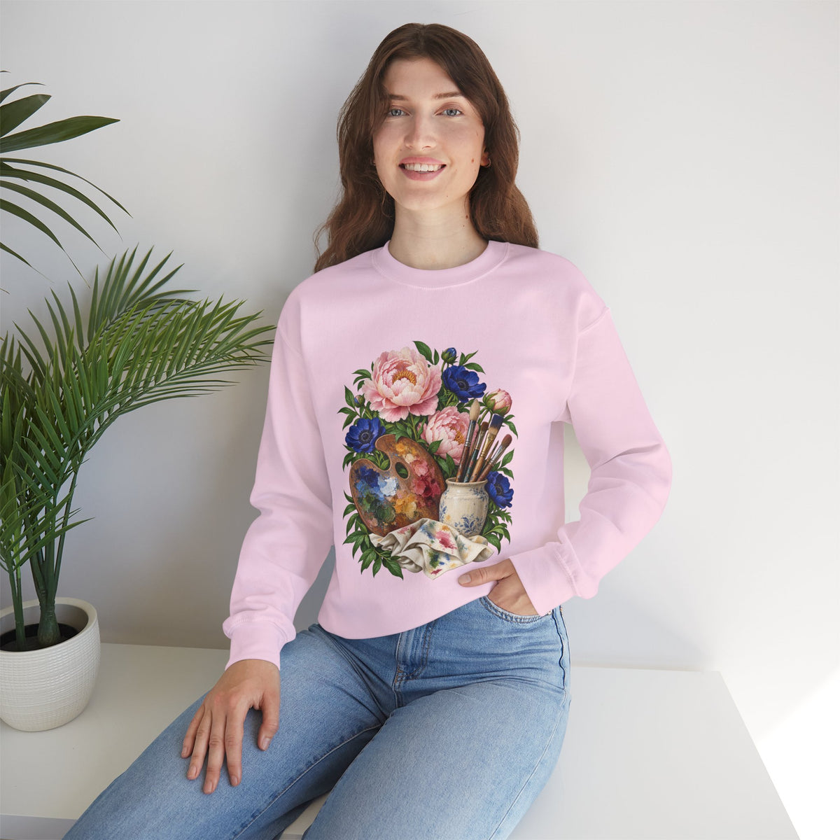 The Colors She Kept crewneck sweatshirt, a paint-covered artist palette beside a cream ceramic jar of brushes with pink peonies and deep blue flowers, image 20 of 28