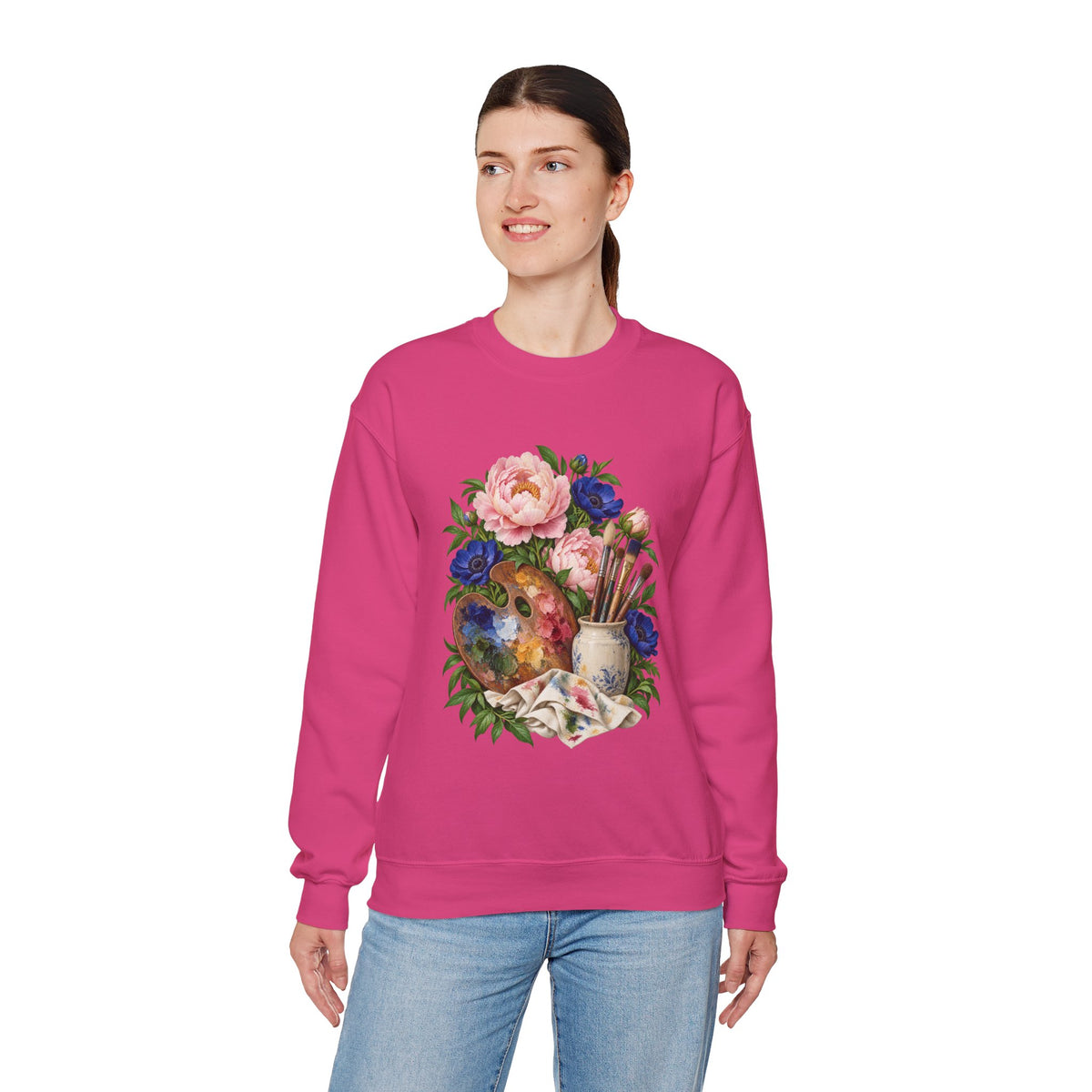 The Colors She Kept crewneck sweatshirt, a paint-covered artist palette beside a cream ceramic jar of brushes with pink peonies and deep blue flowers, image 12 of 28