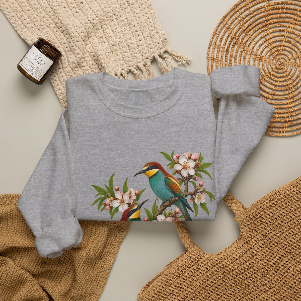The Scenic Way Home sweatshirt — two birds with teal, golden-yellow and rust plumage perched among cream and blush blossoms, on a unisex crewneck