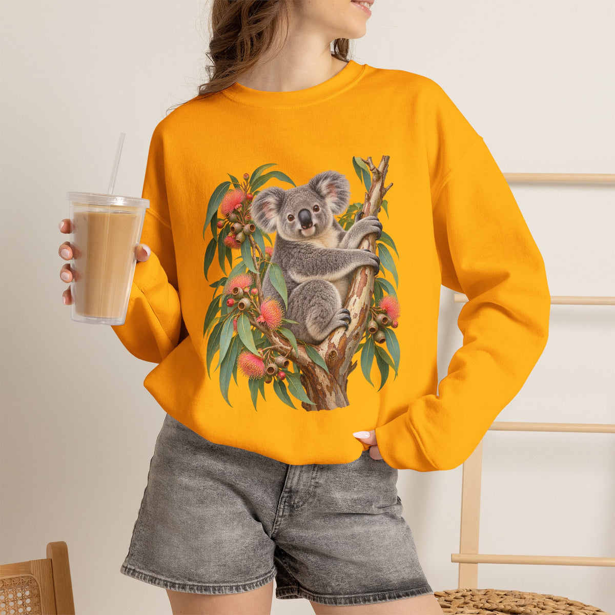 Booked for the Afternoon sweatshirt — a grey koala resting among eucalyptus leaves and coral-pink blossoms, on a unisex crewneck
