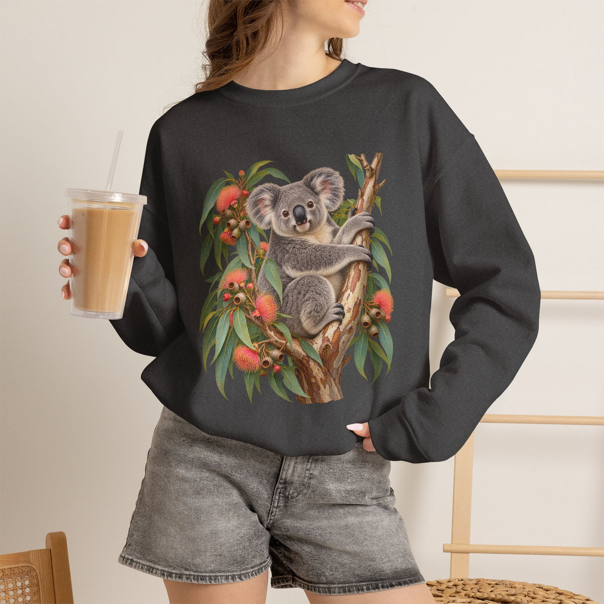 Booked for the Afternoon sweatshirt — a grey koala resting among eucalyptus leaves and coral-pink blossoms, on a unisex crewneck