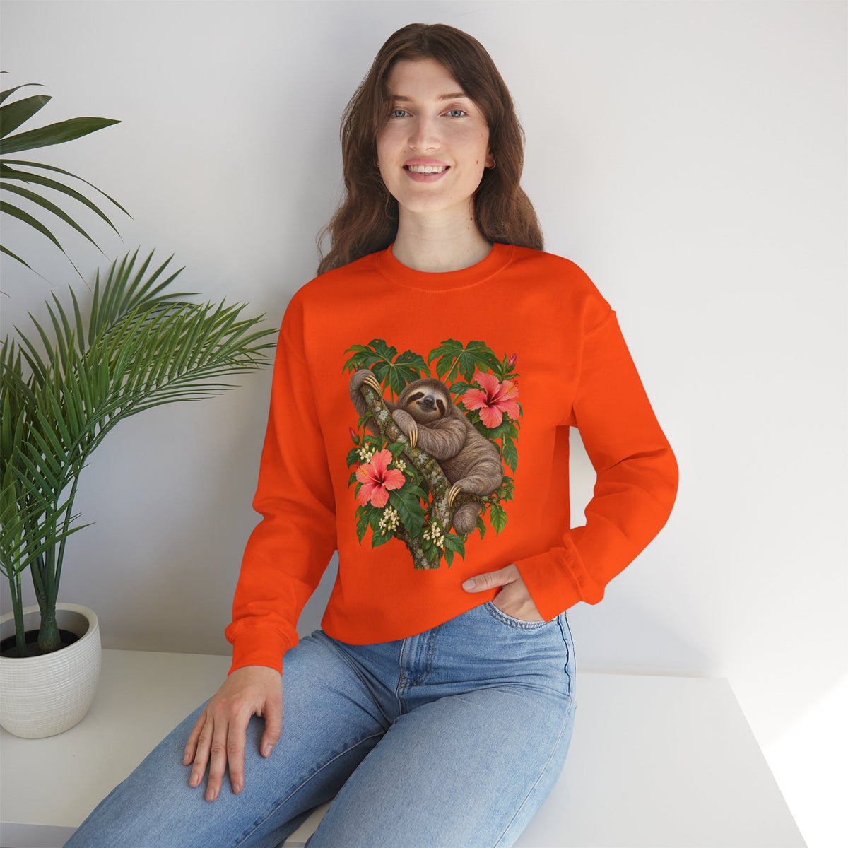 Taking My Sweet Time sweatshirt — a sloth resting on a mossy branch among coral hibiscus, cream blossoms and tropical leaves, on a unisex crewneck