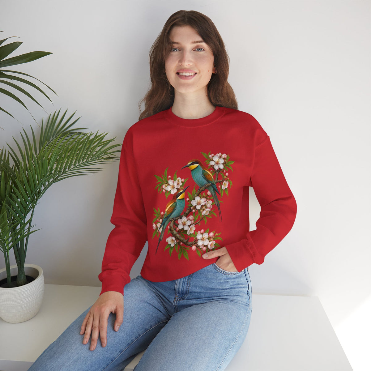 The Scenic Way Home sweatshirt — two birds with teal, golden-yellow and rust plumage perched among cream and blush blossoms, on a unisex crewneck