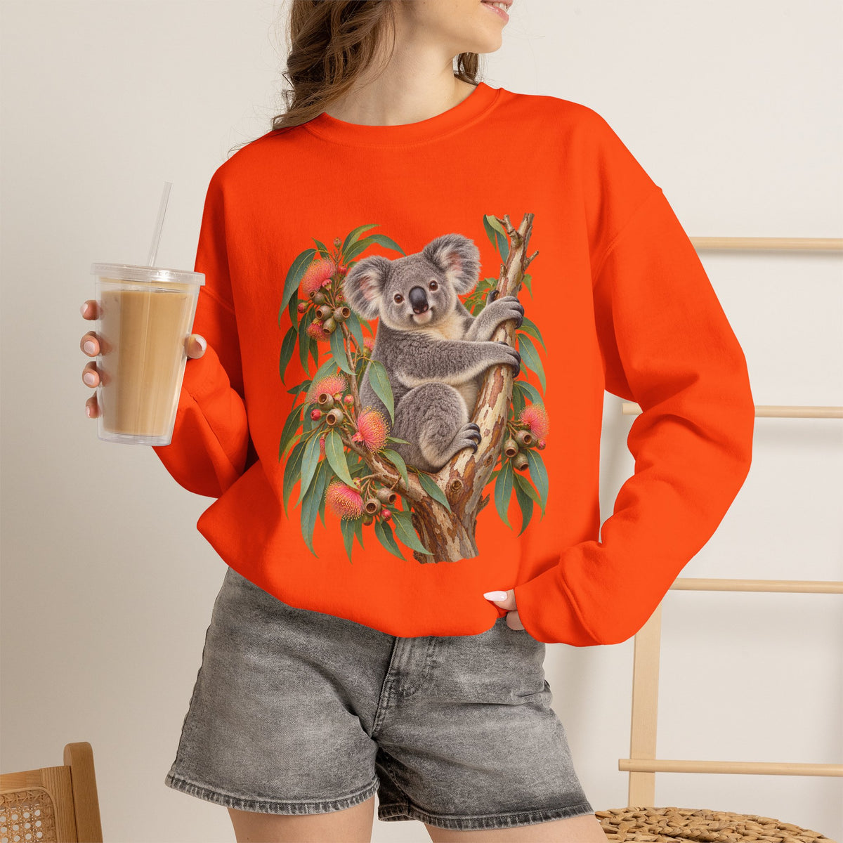 Booked for the Afternoon sweatshirt — a grey koala resting among eucalyptus leaves and coral-pink blossoms, on a unisex crewneck
