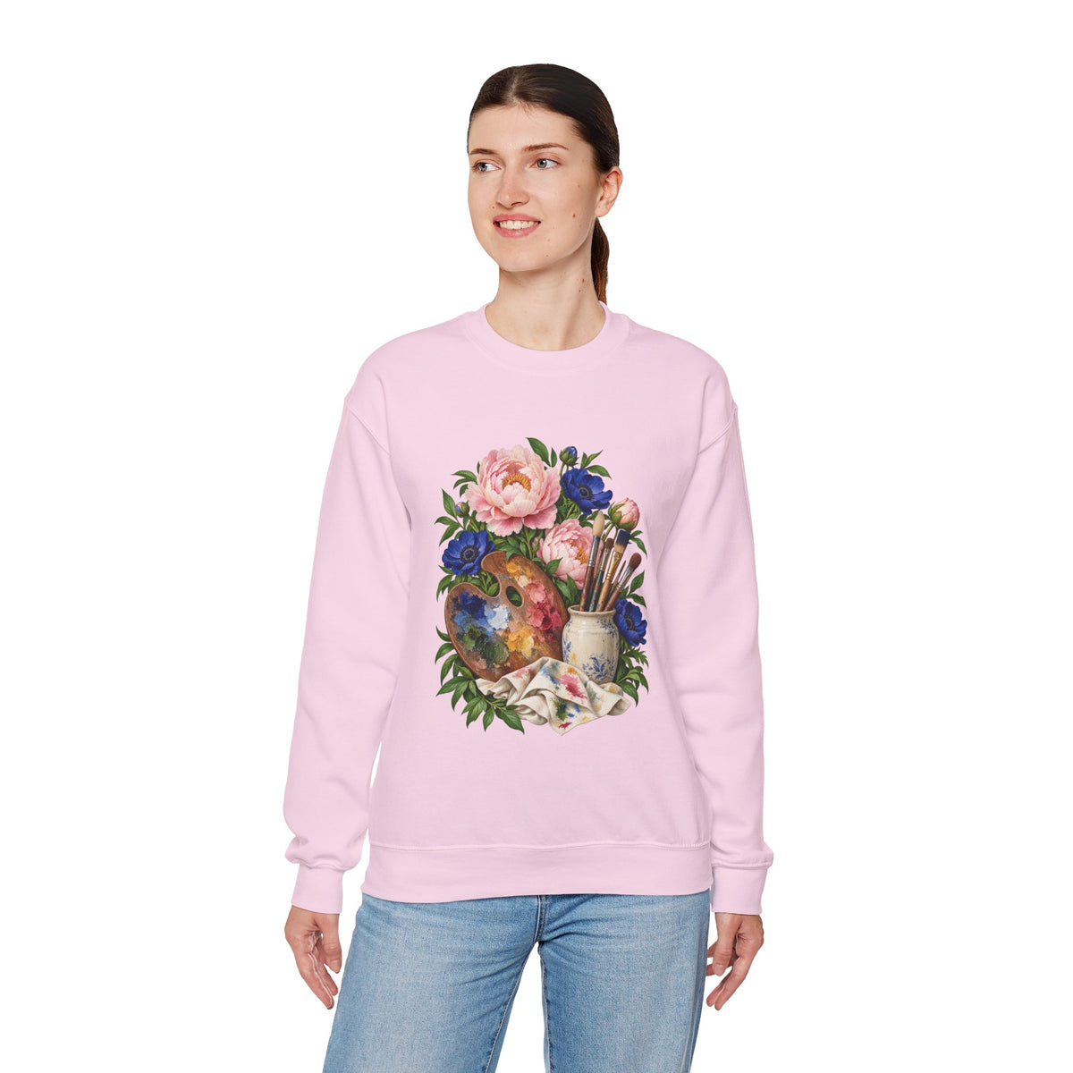 The Colors She Kept crewneck sweatshirt, a paint-covered artist palette beside a cream ceramic jar of brushes with pink peonies and deep blue flowers, image 21 of 28