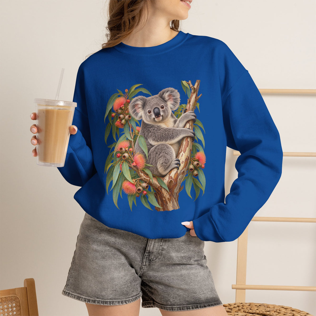 Booked for the Afternoon sweatshirt — a grey koala resting among eucalyptus leaves and coral-pink blossoms, on a unisex crewneck