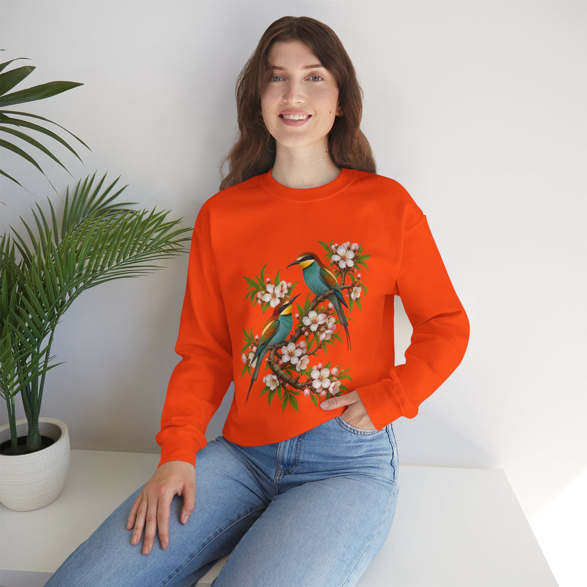 The Scenic Way Home sweatshirt — two birds with teal, golden-yellow and rust plumage perched among cream and blush blossoms, on a unisex crewneck