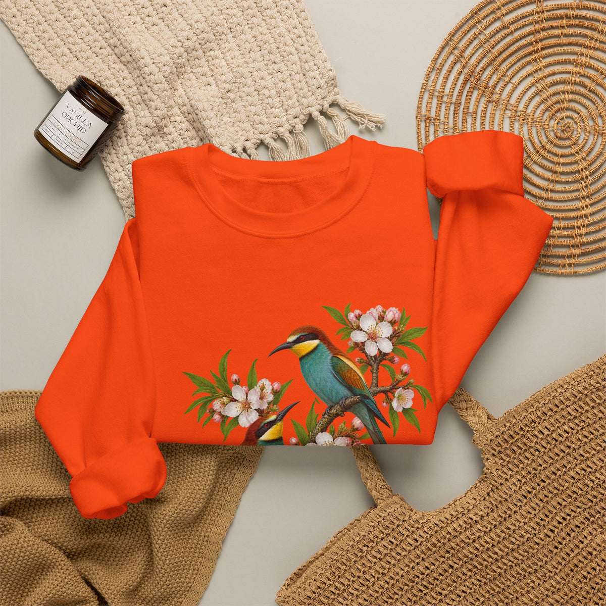 The Scenic Way Home sweatshirt — two birds with teal, golden-yellow and rust plumage perched among cream and blush blossoms, on a unisex crewneck