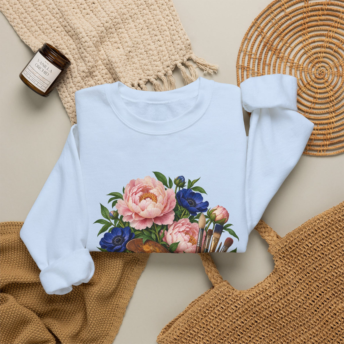 The Colors She Kept crewneck sweatshirt, a paint-covered artist palette beside a cream ceramic jar of brushes with pink peonies and deep blue flowers, image 16 of 28