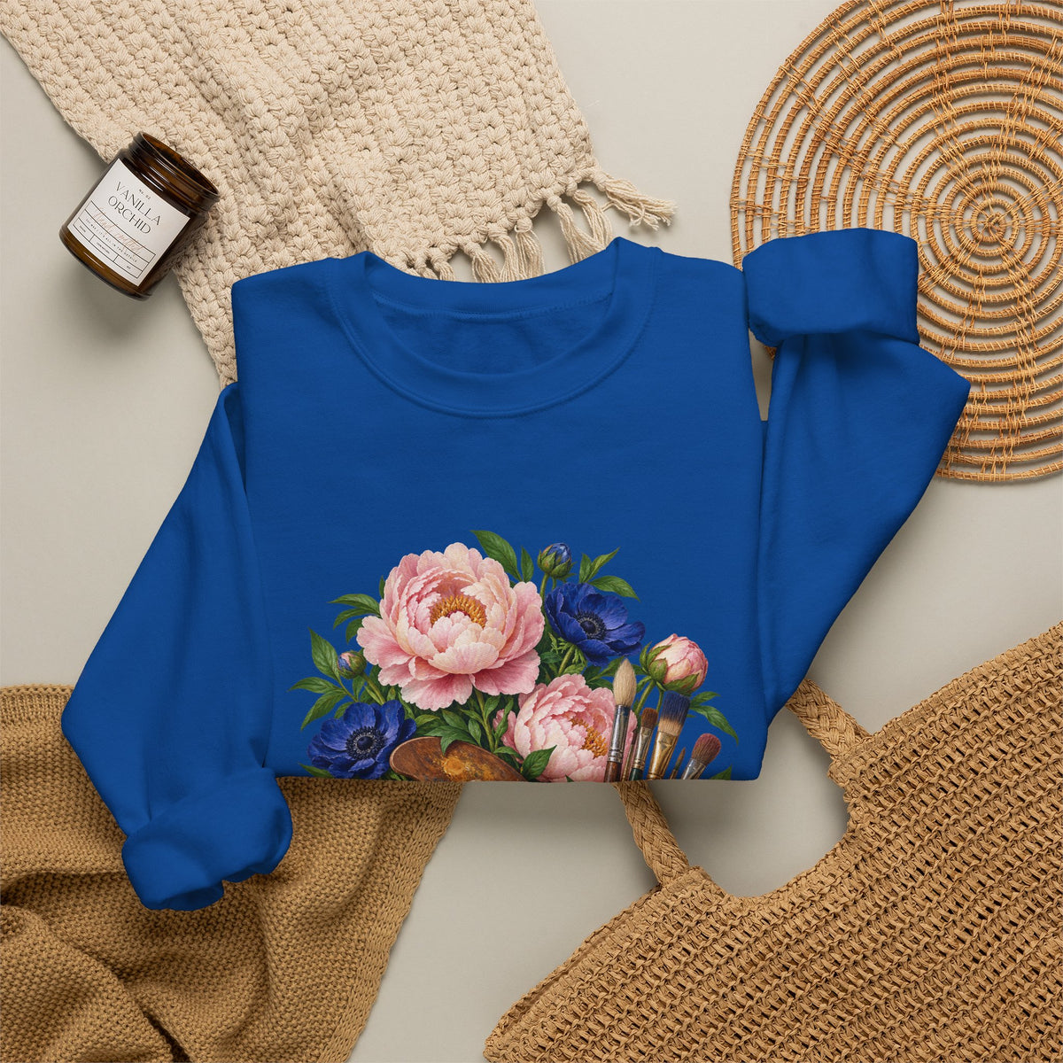 The Colors She Kept crewneck sweatshirt, a paint-covered artist palette beside a cream ceramic jar of brushes with pink peonies and deep blue flowers, image 27 of 28