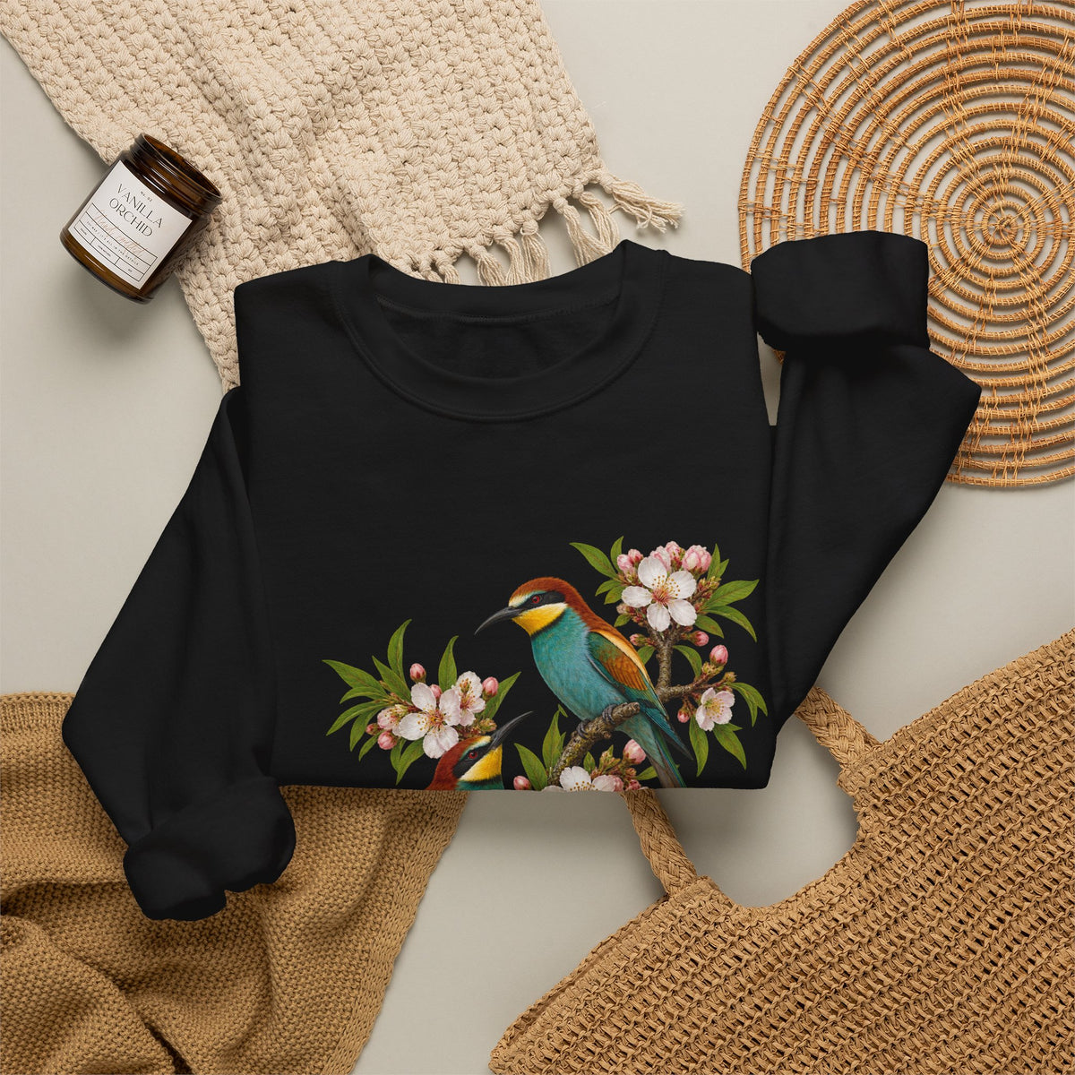 The Scenic Way Home sweatshirt — two birds with teal, golden-yellow and rust plumage perched among cream and blush blossoms, on a unisex crewneck