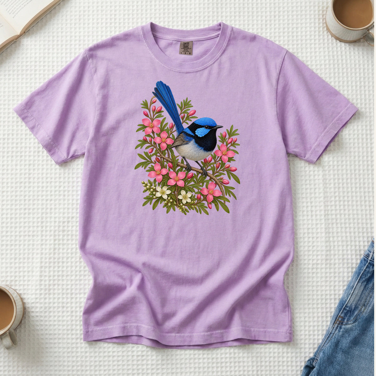 Small blue and black bird with an upright tail among pink blossoms and cream flowers, printed on an Orchid lavender Comfort Colors 1717 unisex t-shirt
