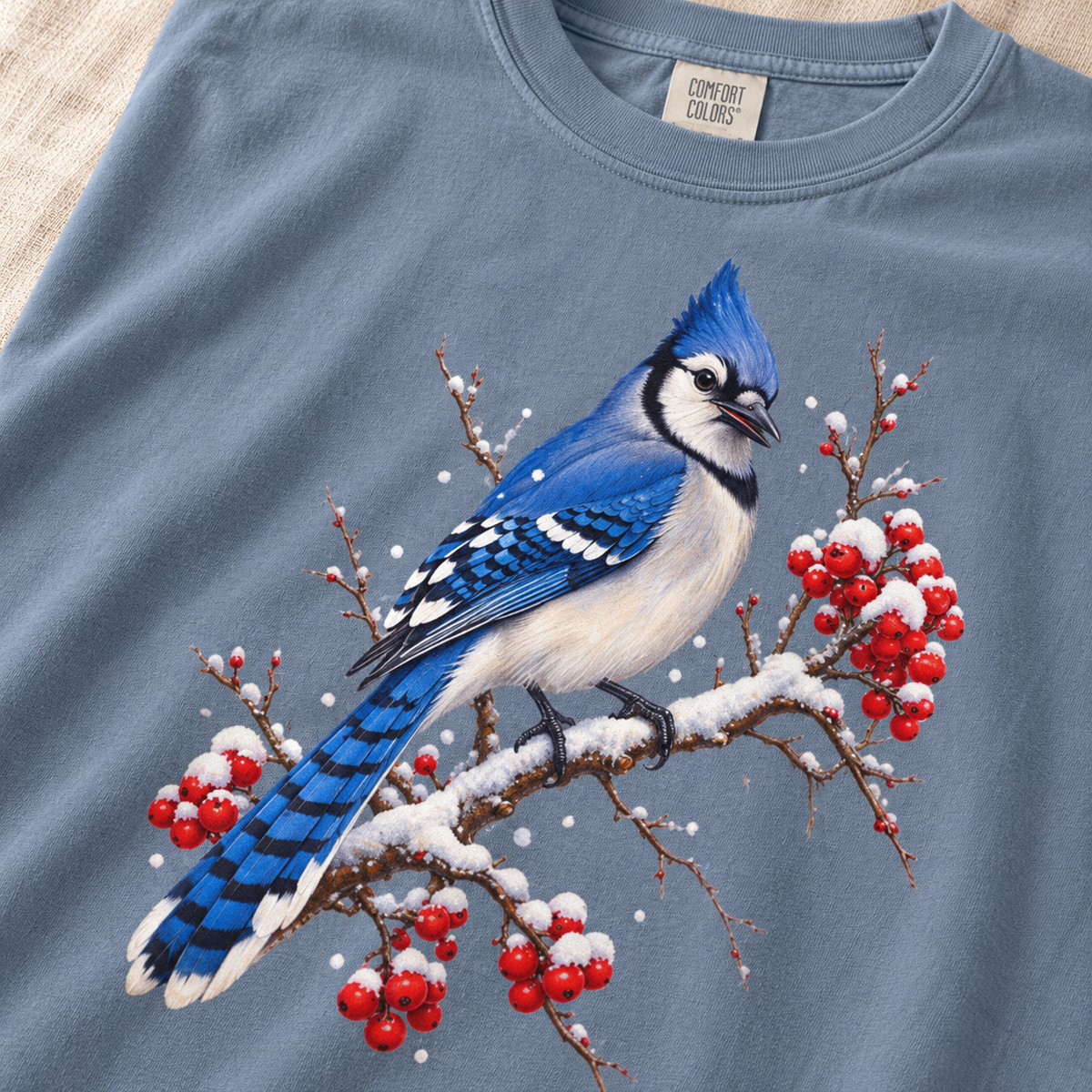 Close-up of the blue jay winterberry print – crest, black necklace, white wing bars and red berries under snow on garment-dyed cotton