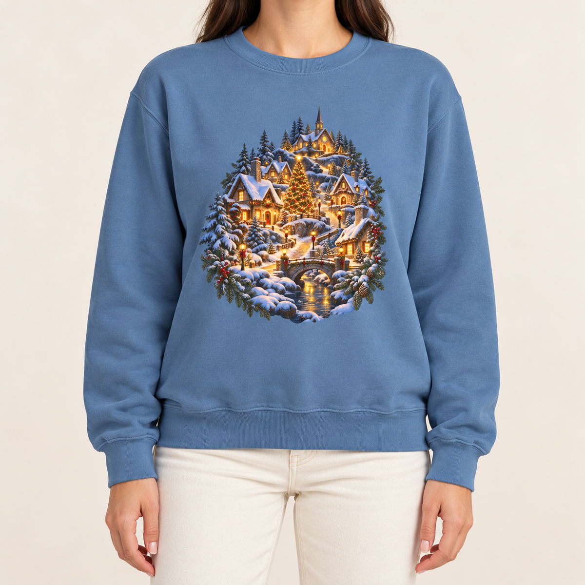 Small town Christmas sweatshirt in Blue Jean: a snowy hillside village with a lit church, Christmas tree and stone bridge, on a light washed denim garment-dyed Comfort Colors crewneck