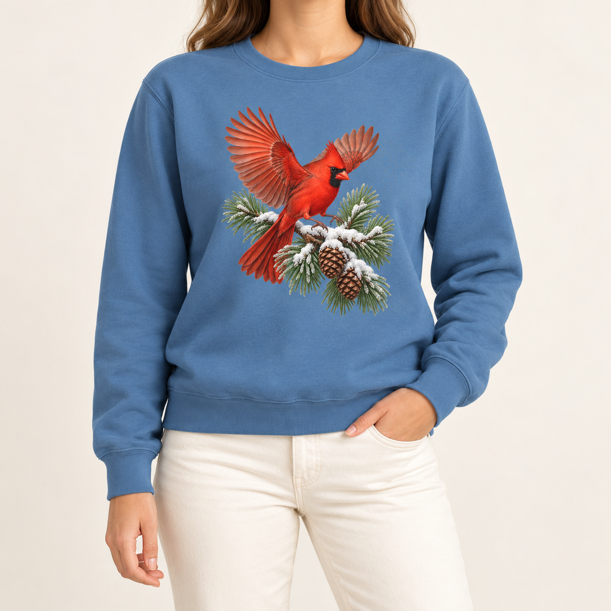 Cardinal in flight sweatshirt in Blue Jean – a male northern cardinal with wings spread landing on a snow-covered pine bough with pinecones, printed large on the chest of a Comfort Colors crewneck