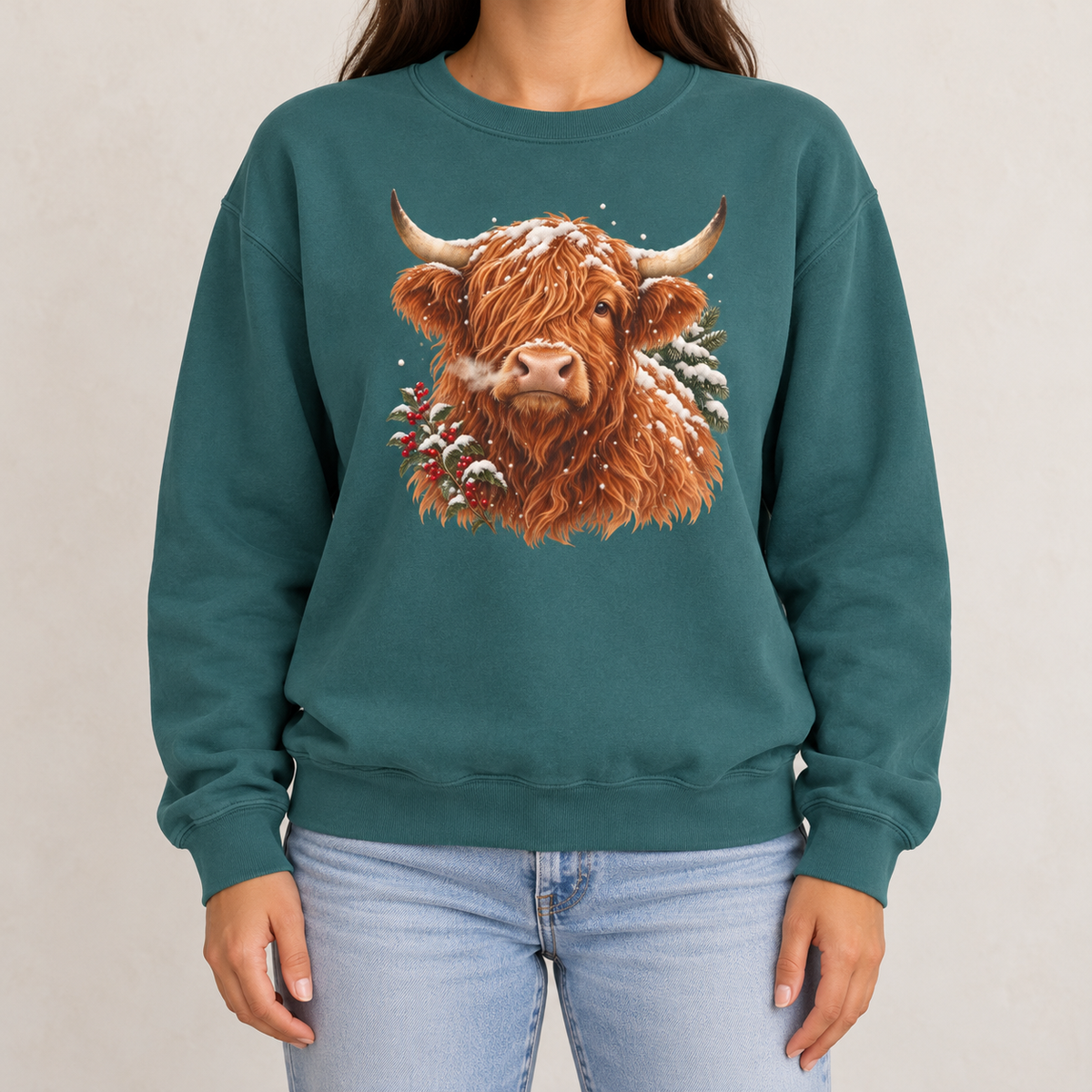 Highland cow winter sweatshirt in Blue Spruce worn with jeans – snowy Highland cow portrait with pine and red berries on a garment-dyed Comfort Colors crewneck