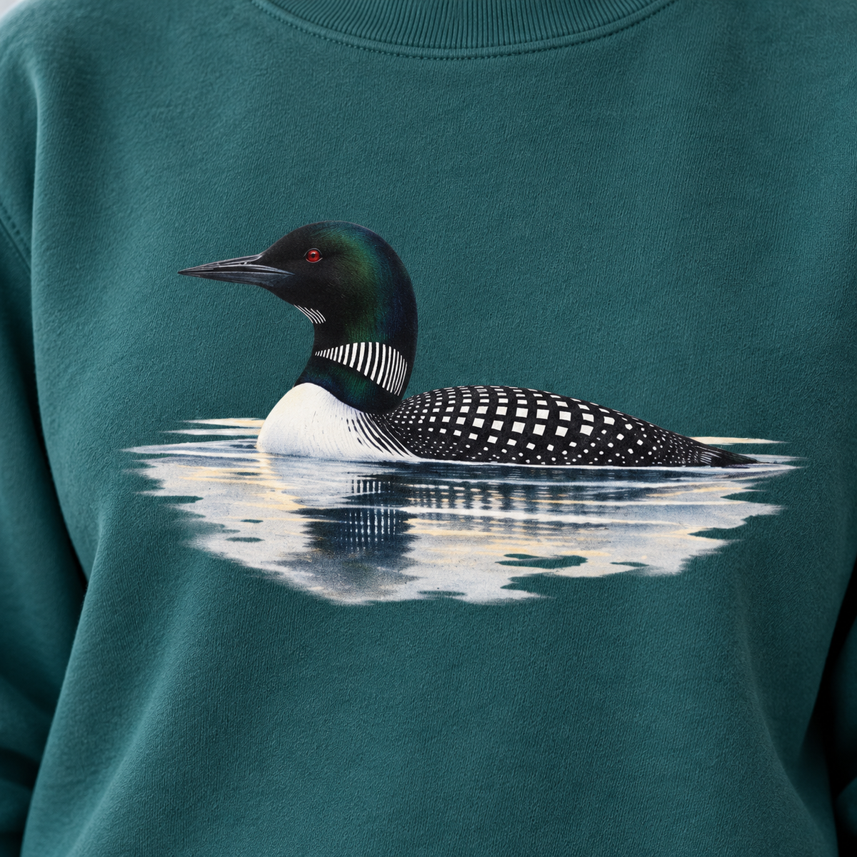 Close-up of the common loon print on a Blue Spruce garment-dyed Comfort Colors sweatshirt - the loon low in the water with mist behind it