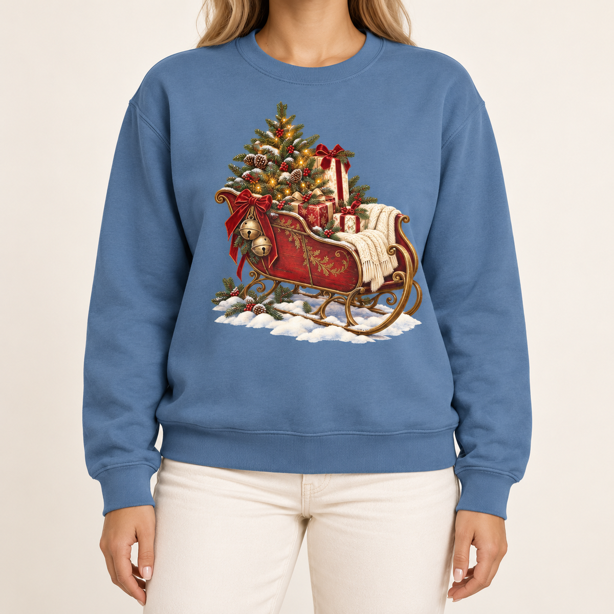 Vintage Christmas sleigh sweatshirt in Blue Jean – a cranberry-red sleigh with gold trim heaped with fresh-cut fir and hung with golden bells, printed large on the chest of a Comfort Colors crewneck