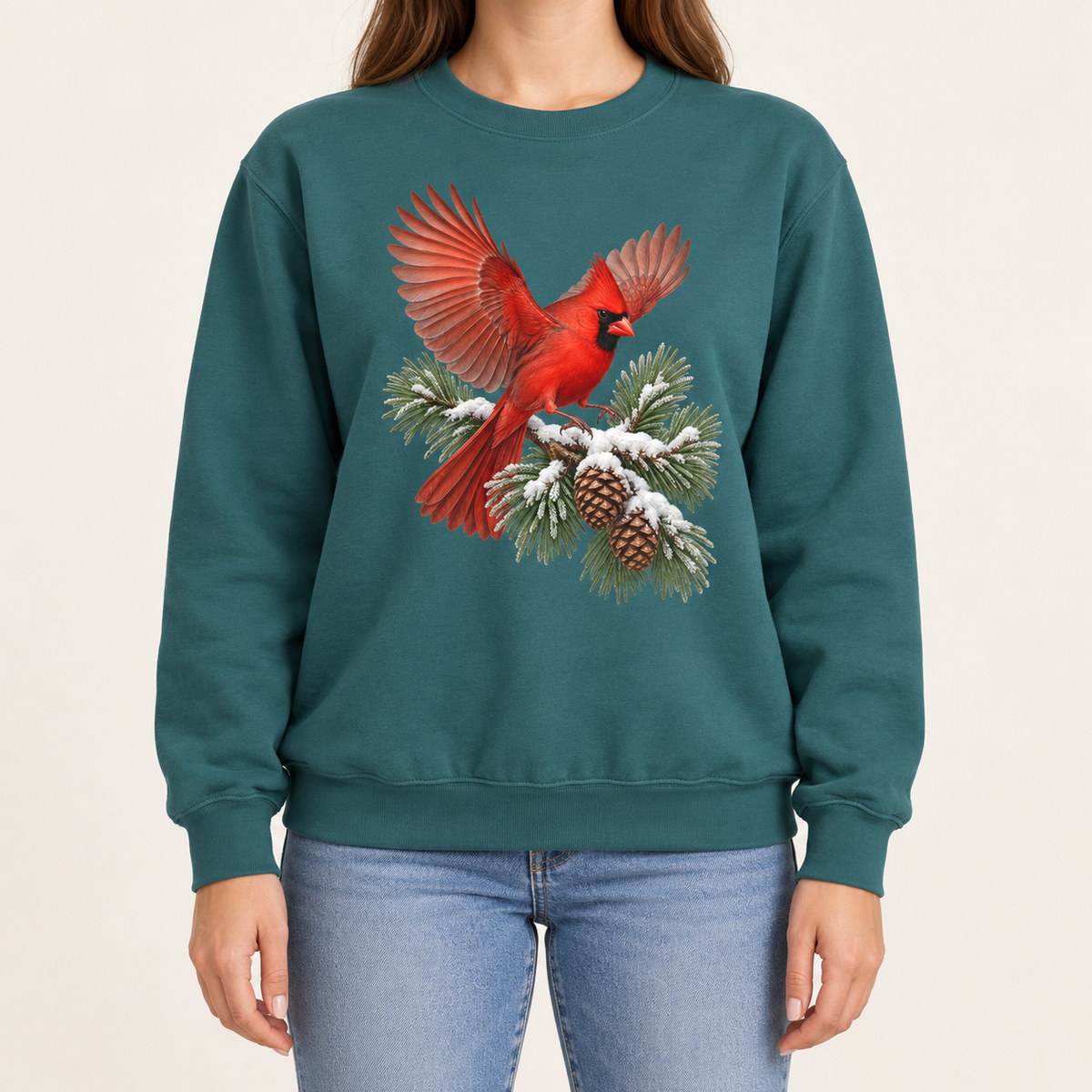 Cardinal in flight sweatshirt in Blue Spruce – a male northern cardinal with wings spread landing on a snow-covered pine bough with pinecones, printed large on the chest of a Comfort Colors crewneck