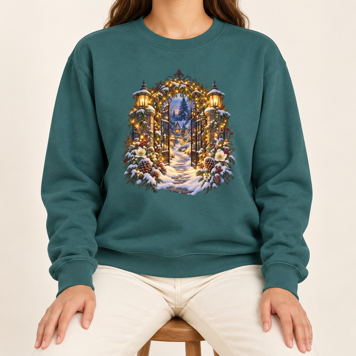 Christmas garden gate sweatshirt in Blue Spruce: an open iron gate with lantern-topped pillars and a snowy path to a lit cottage, on a deep forest green garment-dyed Comfort Colors crewneck