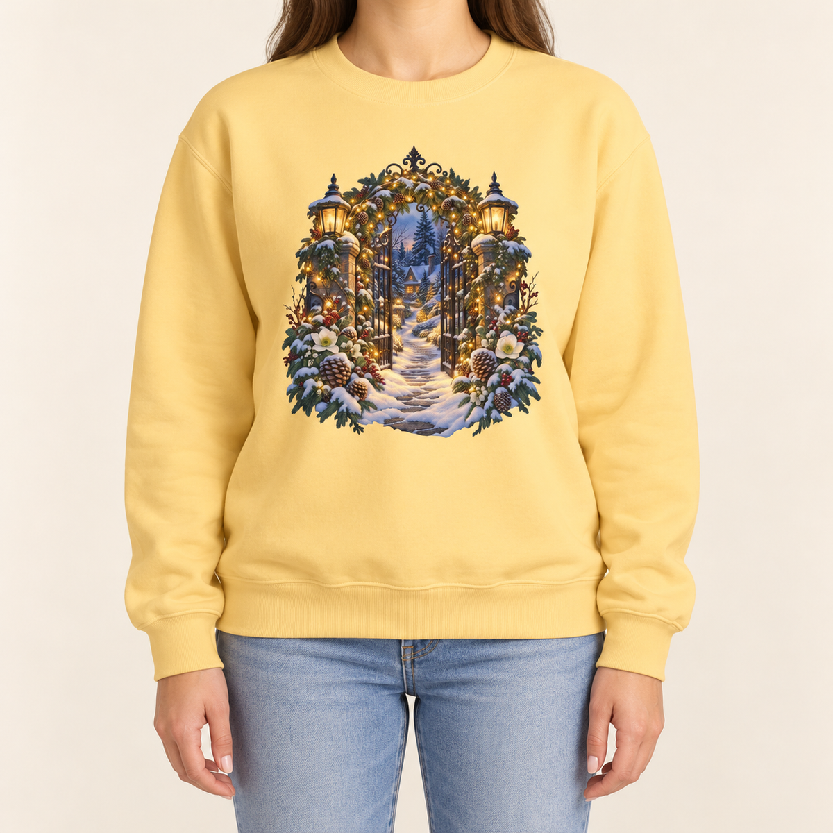 Christmas garden gate sweatshirt in Butter: an open iron gate with lantern-topped pillars and a snowy path to a lit cottage, on a soft pale yellow garment-dyed Comfort Colors crewneck