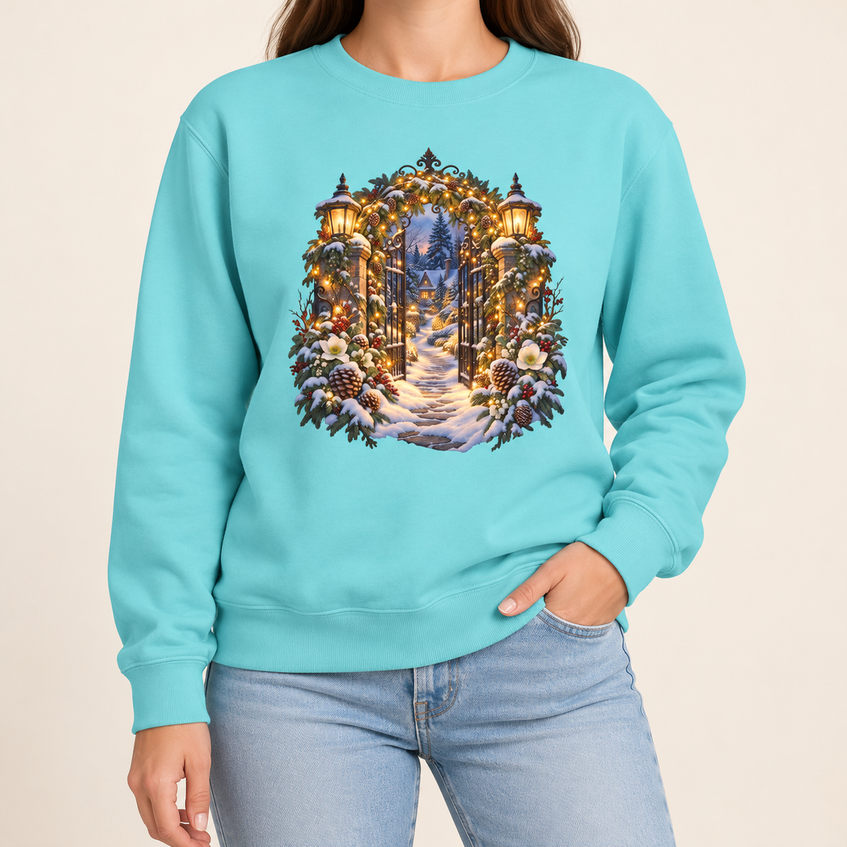 Christmas garden gate sweatshirt in Chalky Mint: an open iron gate with lantern-topped pillars and a snowy path to a lit cottage, on a pale soft mint garment-dyed Comfort Colors crewneck
