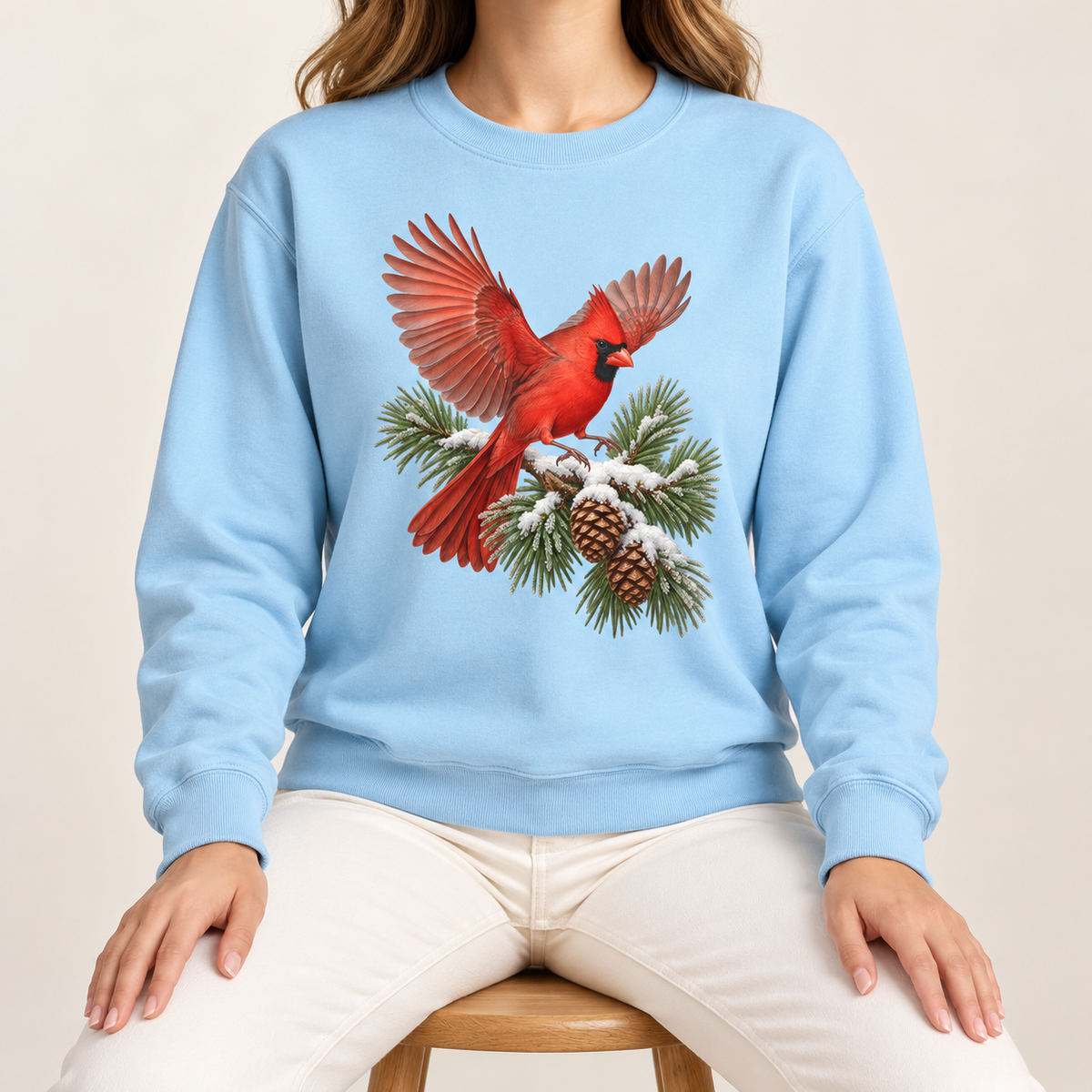 Cardinal in flight sweatshirt in Chambray – a male northern cardinal with wings spread landing on a snow-covered pine bough with pinecones, printed large on the chest of a Comfort Colors crewneck