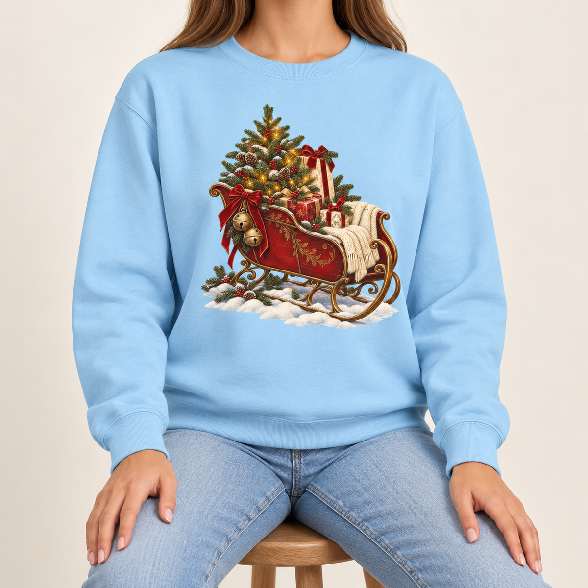 Vintage Christmas sleigh sweatshirt in Chambray – a cranberry-red sleigh with gold trim heaped with fresh-cut fir and hung with golden bells, printed large on the chest of a Comfort Colors crewneck