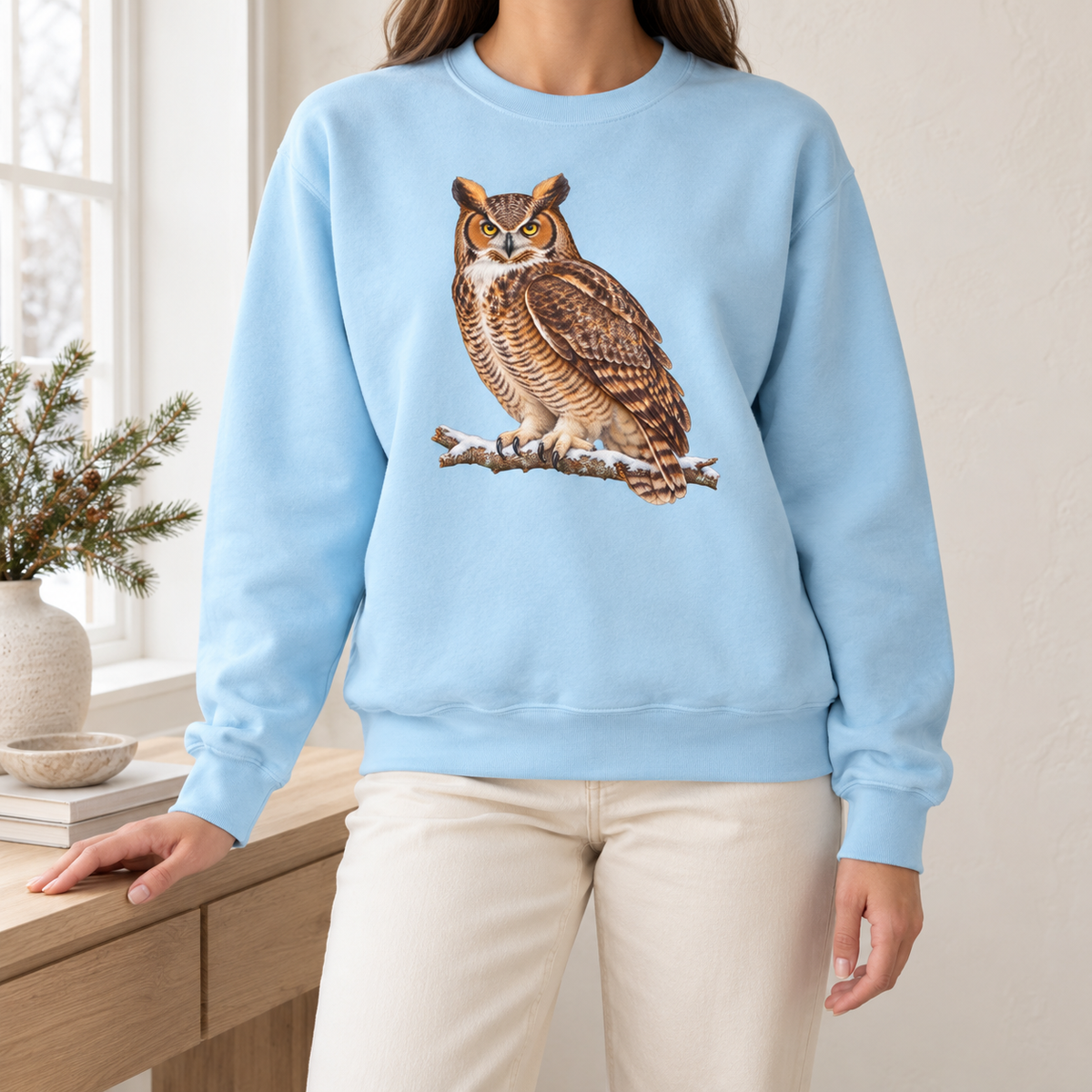 Great horned owl sweatshirt in Chambray worn by a woman – a watercolor great horned owl with ear tufts and yellow eyes on a snowy branch, printed large on a garment-dyed Comfort Colors crewneck