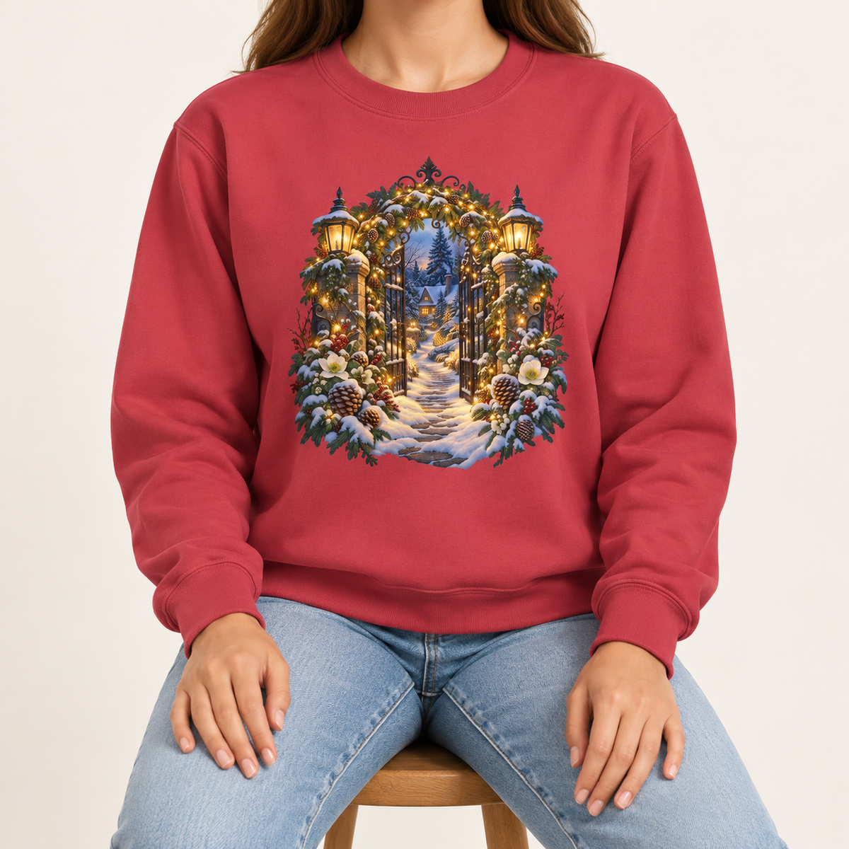 Christmas garden gate sweatshirt in Crimson: an open iron gate with lantern-topped pillars and a snowy path to a lit cottage, on a deep red garment-dyed Comfort Colors crewneck