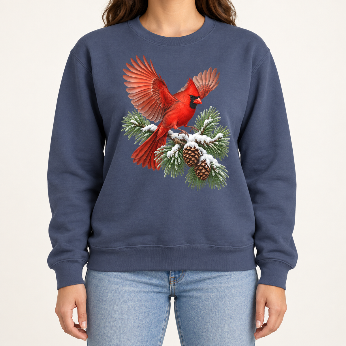 Cardinal in flight sweatshirt in Denim – a male northern cardinal with wings spread landing on a snow-covered pine bough with pinecones, printed large on the chest of a Comfort Colors crewneck